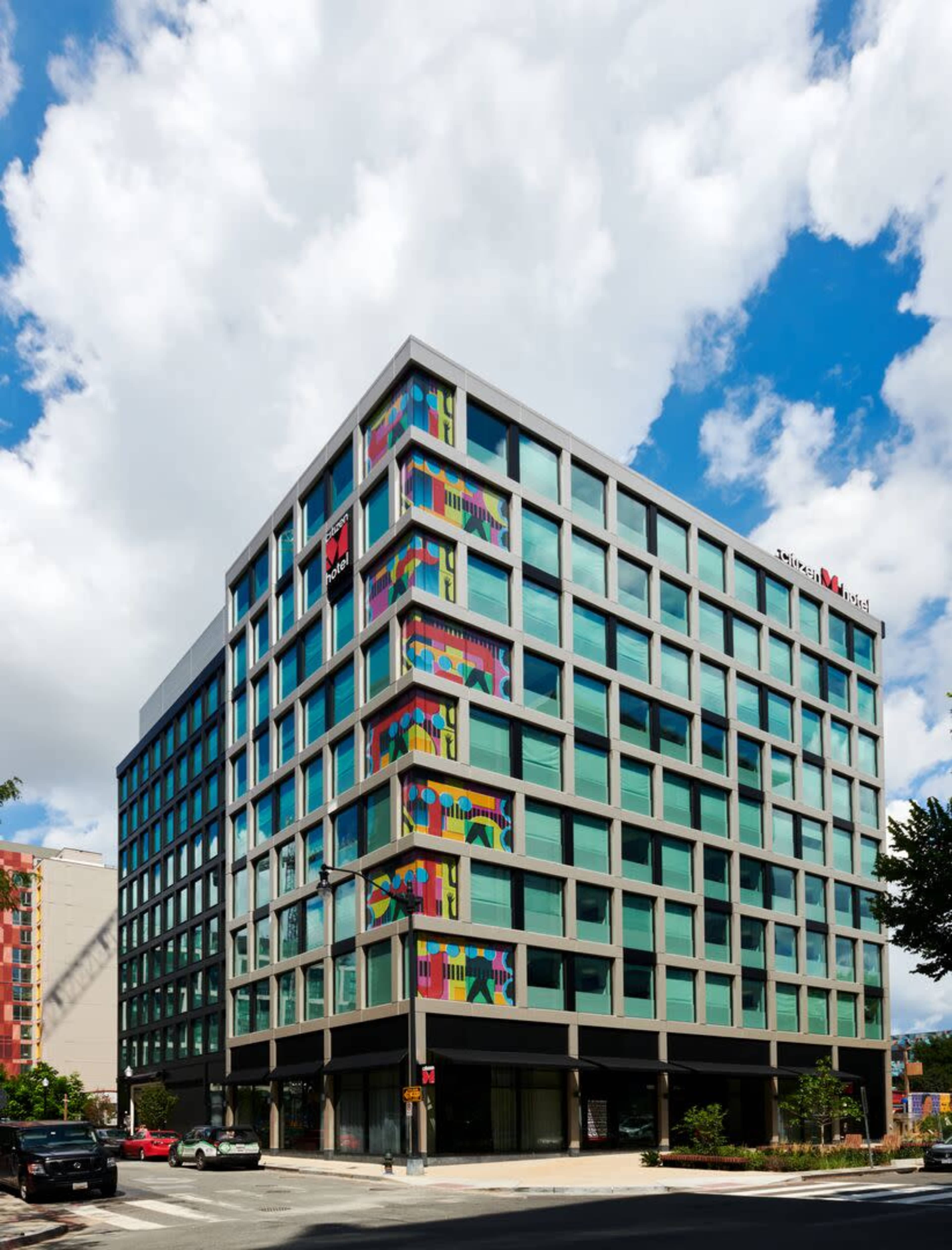 A modern multi-story hotel building features large glass windows and colorful murals on its facade.