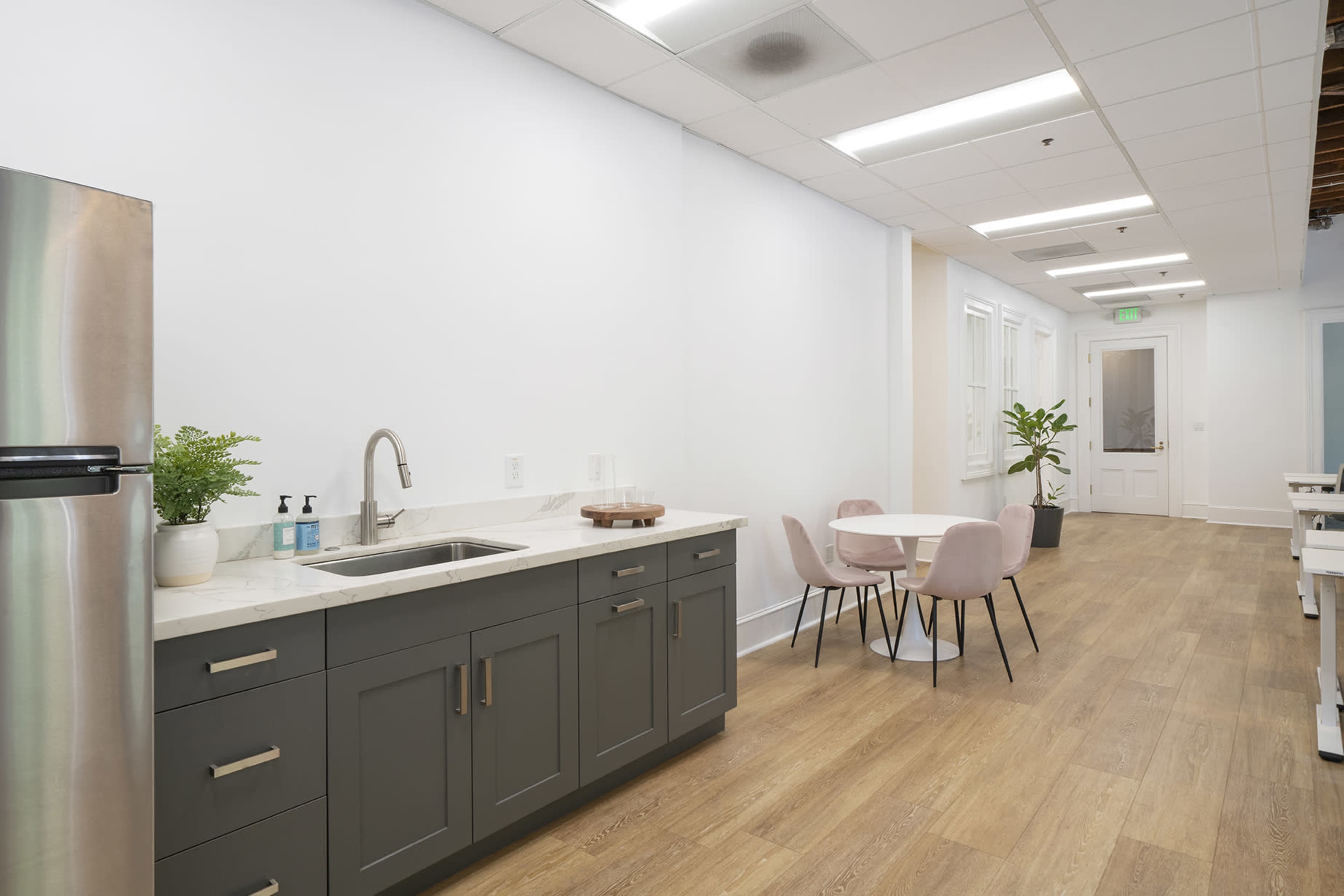 A modern kitchen area with a sink, gray cabinets, and a small round dining table surrounded by pink chairs.