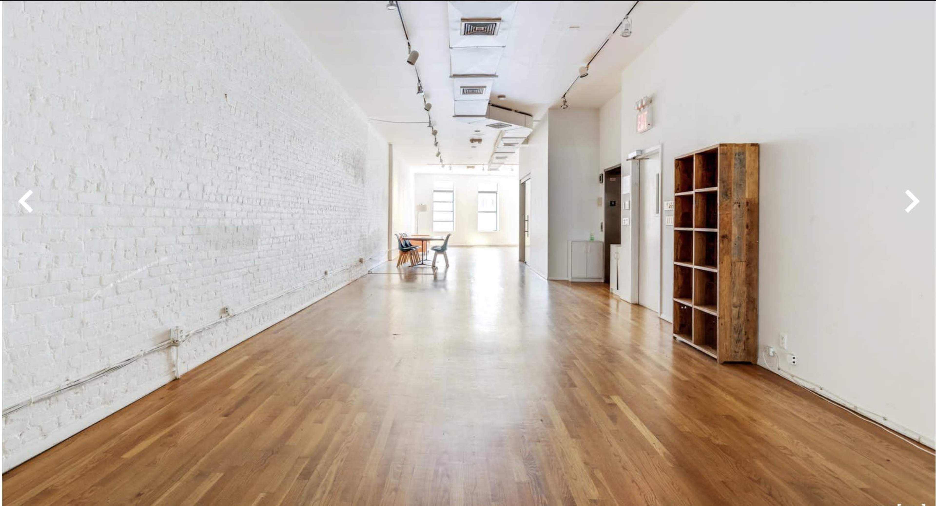 A spacious, empty room with hardwood floors, white walls, and a few pieces of furniture against one side.