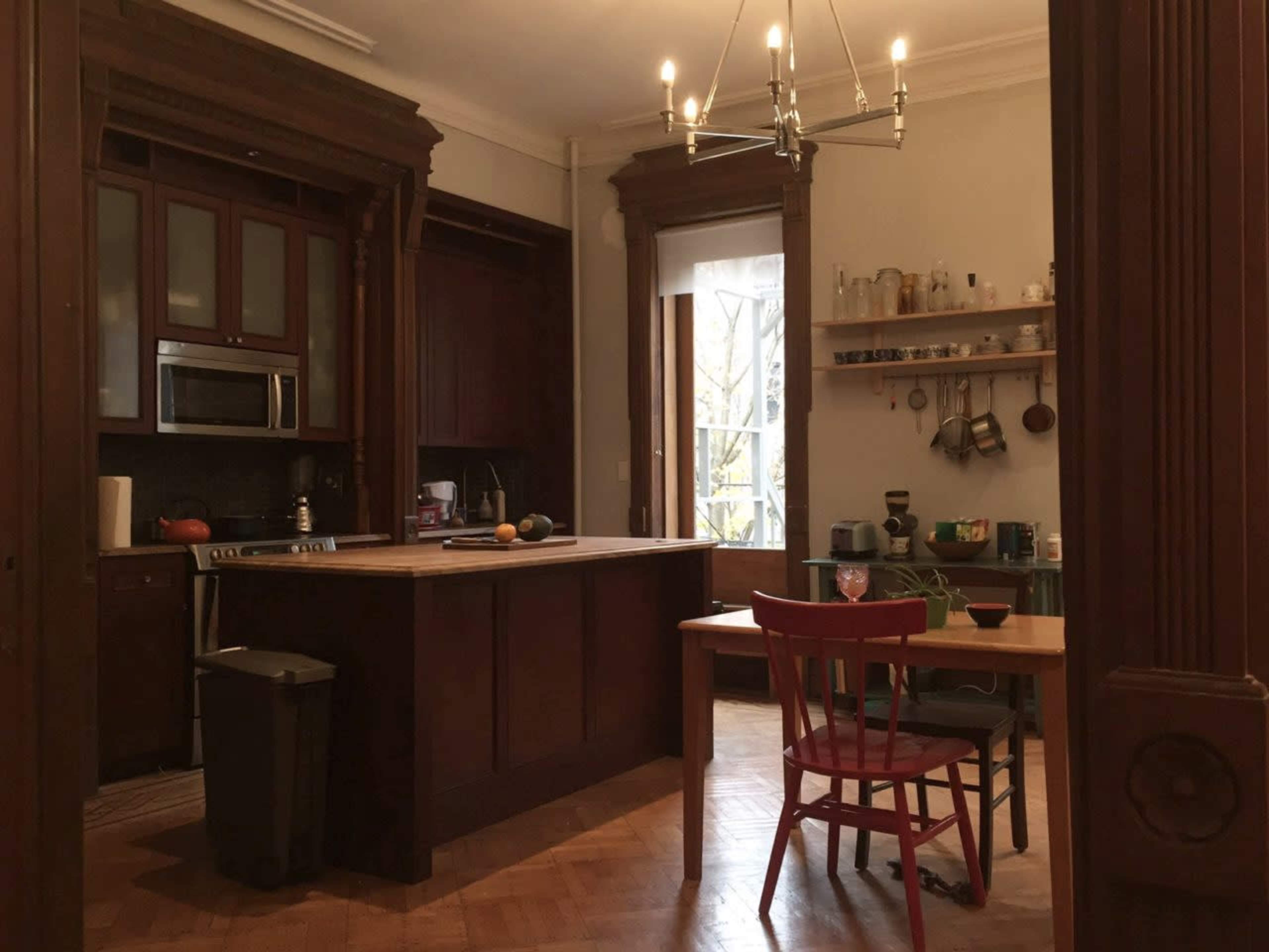 A kitchen with dark wood cabinetry, a central island, a dining table with a red chair, and various kitchen items displayed on shelves.