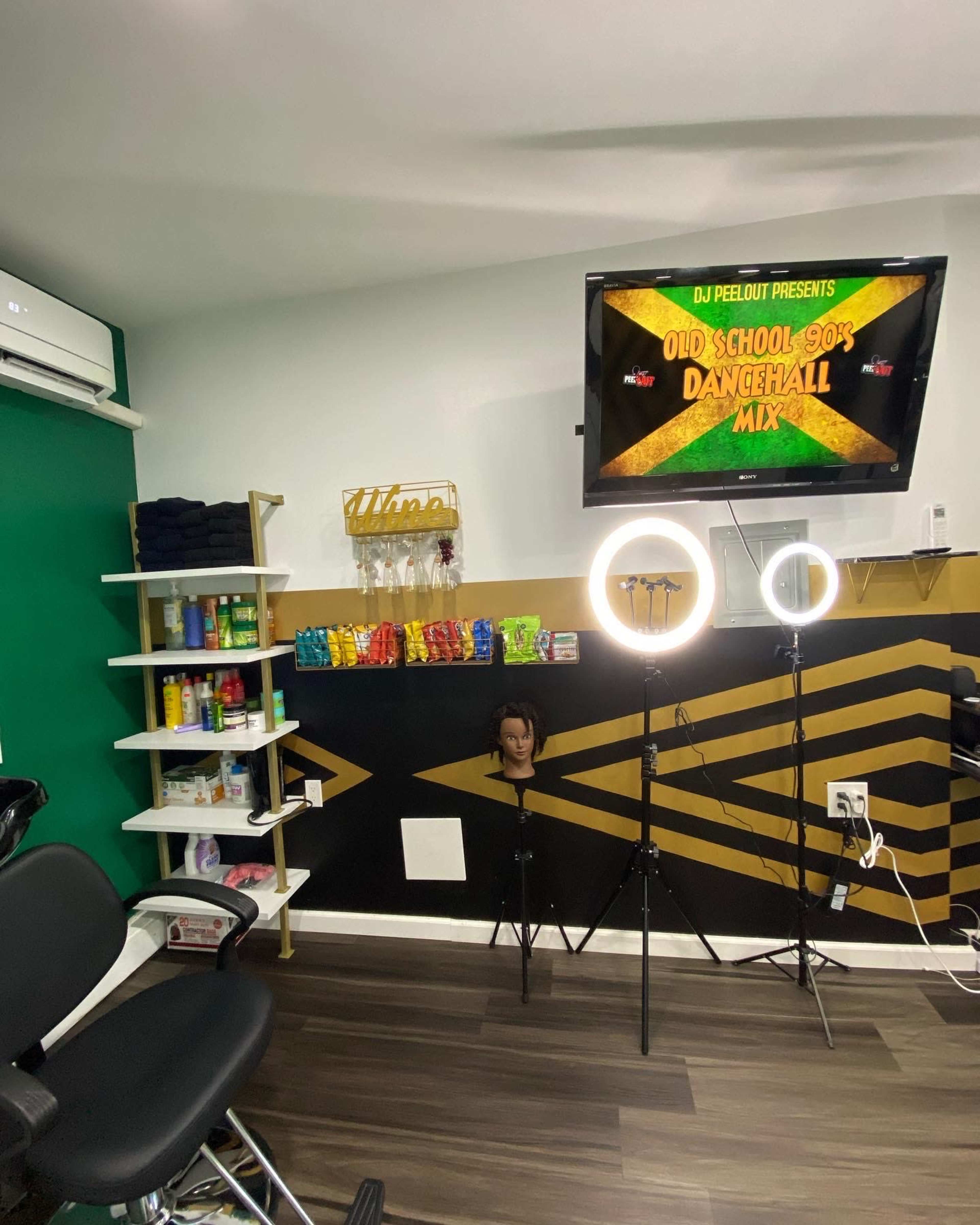 A hair salon interior with a television displaying a music mix, a styling chair, a mannequin head, and organized shelves of hair products.
