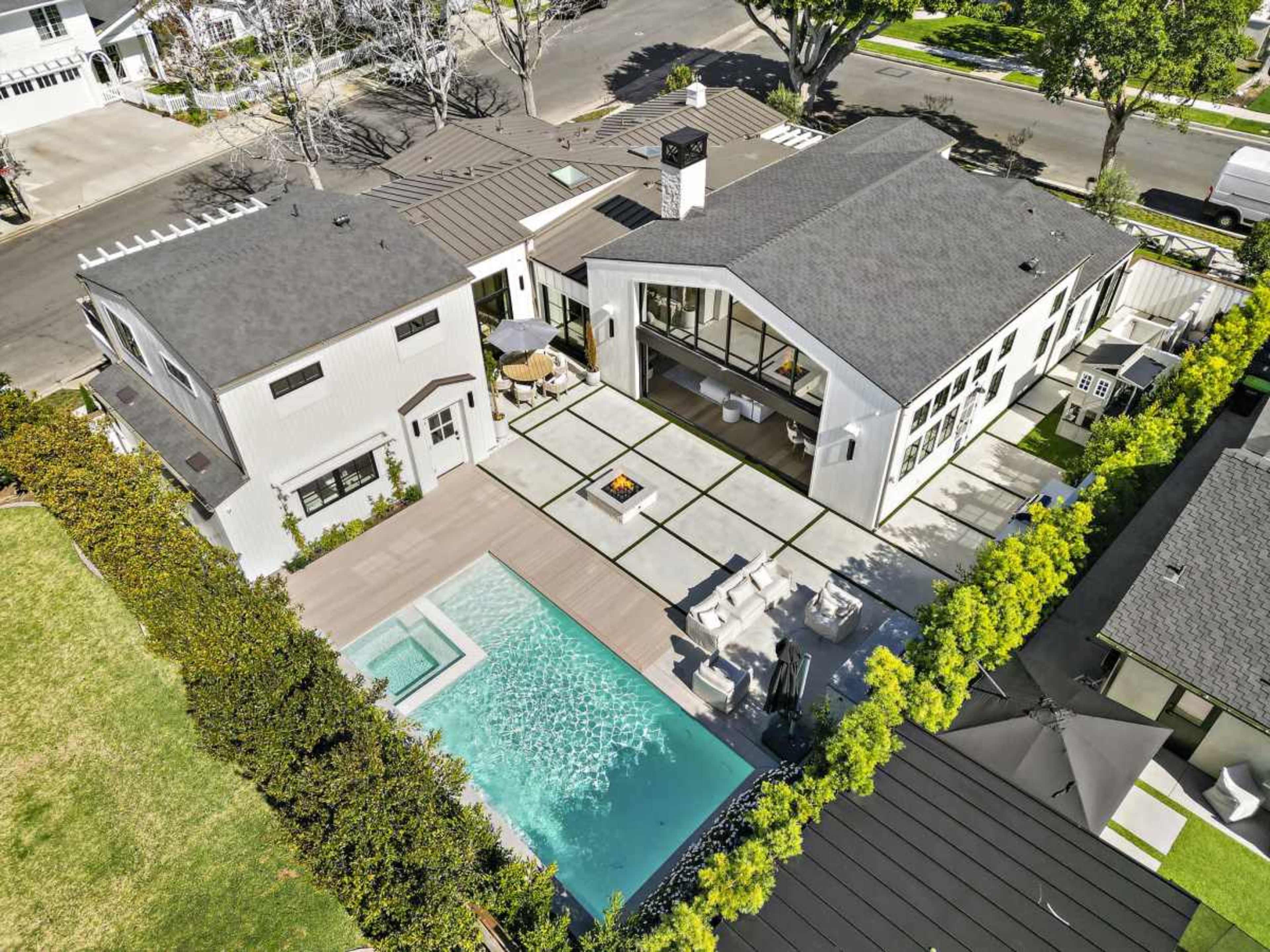The image shows a modern residential property with a swimming pool, outdoor seating area, and a landscaped yard, all viewed from an aerial perspective.