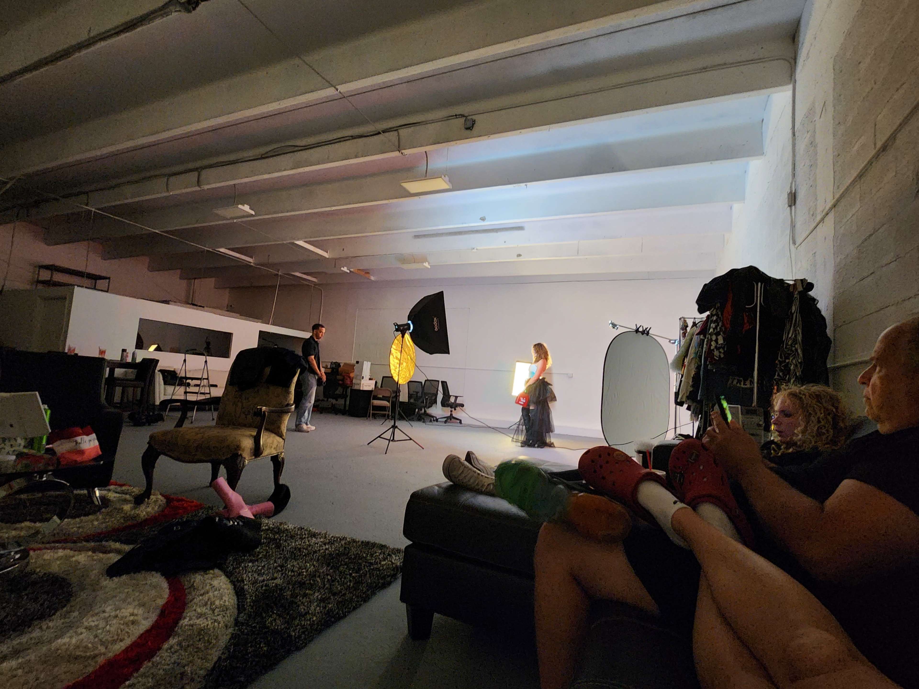A model poses in front of a backdrop while a photographer and an assistant work in a well-lit studio.