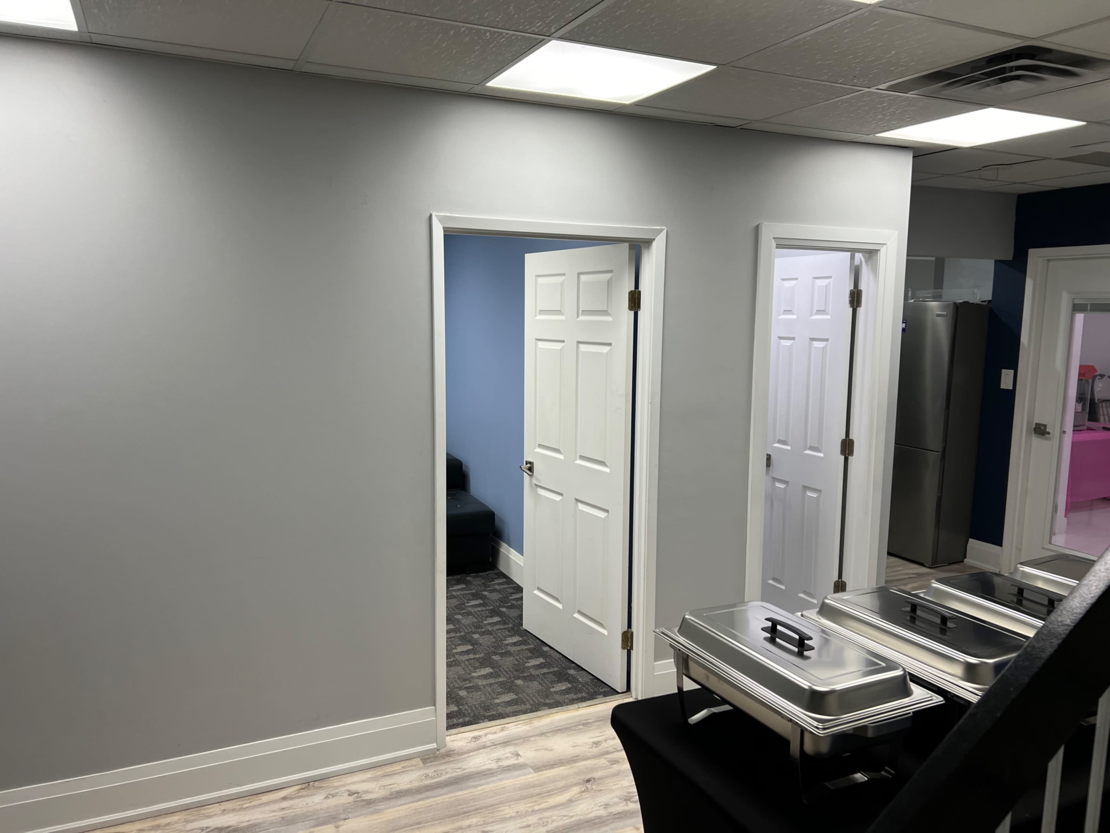 A well-lit office space featuring two white doors, a gray wall, and a stainless steel food cart on a table.