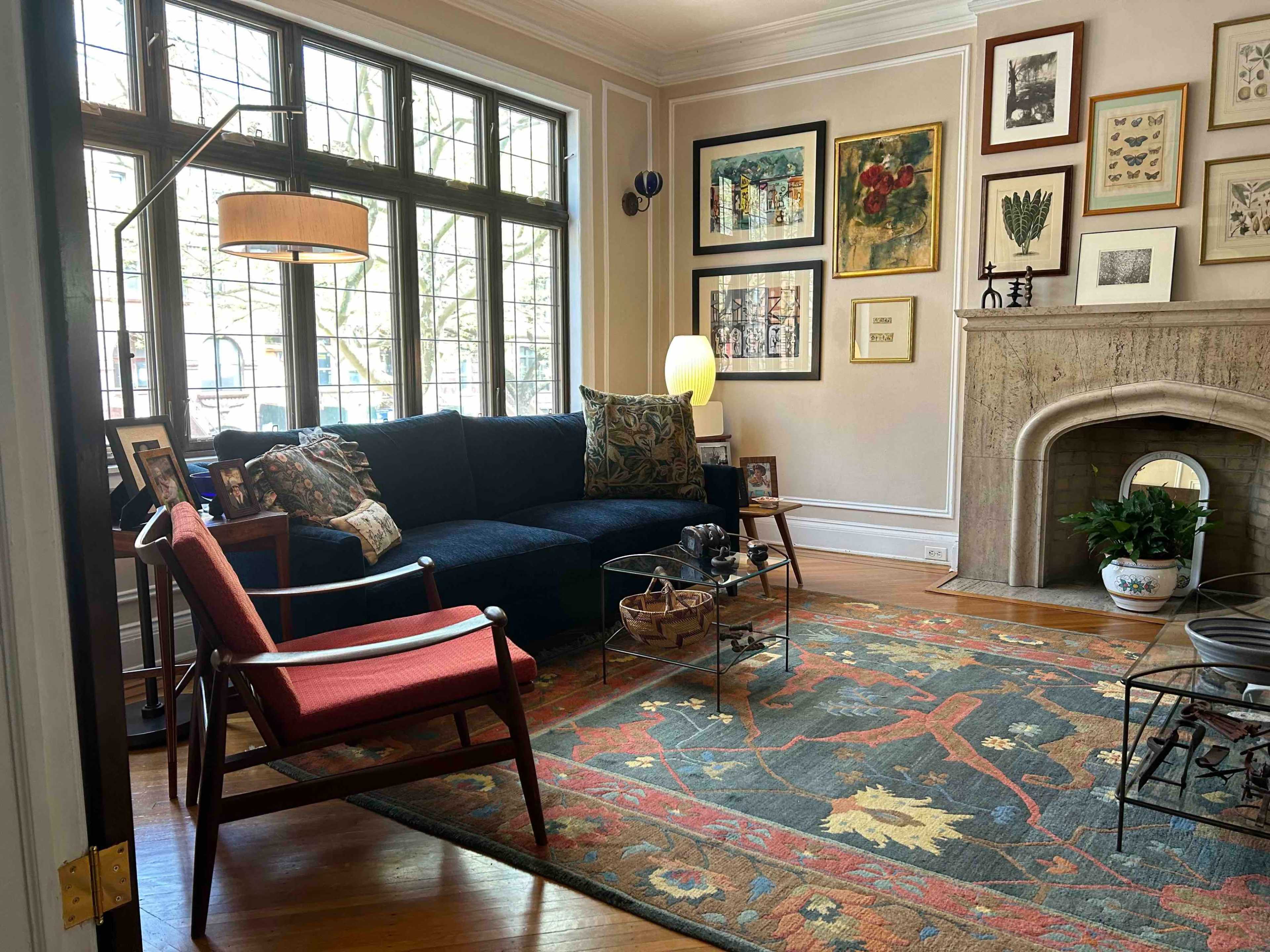 A cozy living room with a dark blue sofa, a red accent chair, and various framed artworks on the walls.