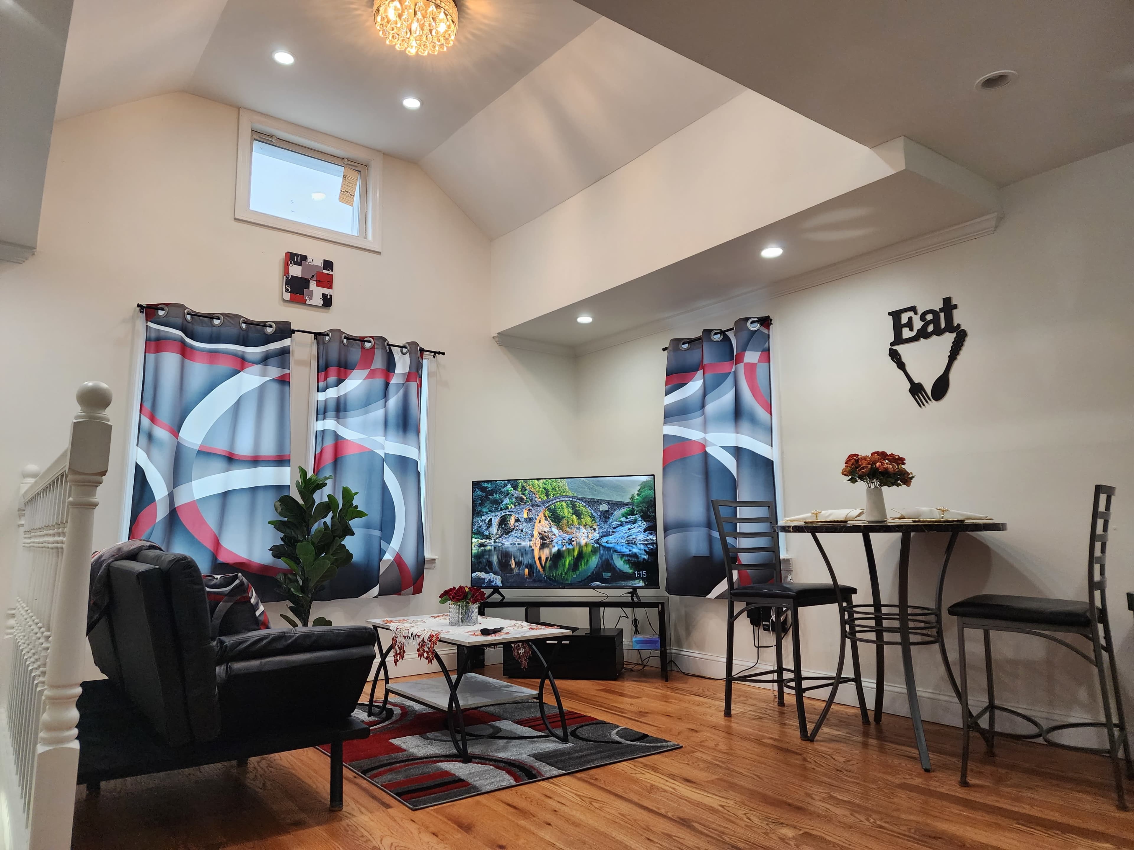 The room features a living area with a sofa, a glass table, and a television against a wall decorated with curtains and wall art.