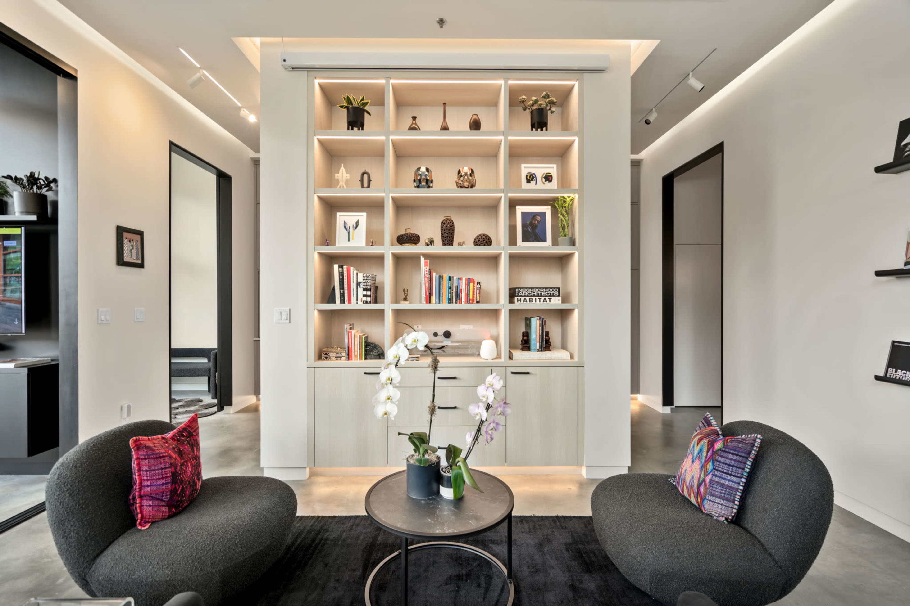 A modern lounge area with a shelf displaying decorative items and books, flanked by two circular chairs and a coffee table.