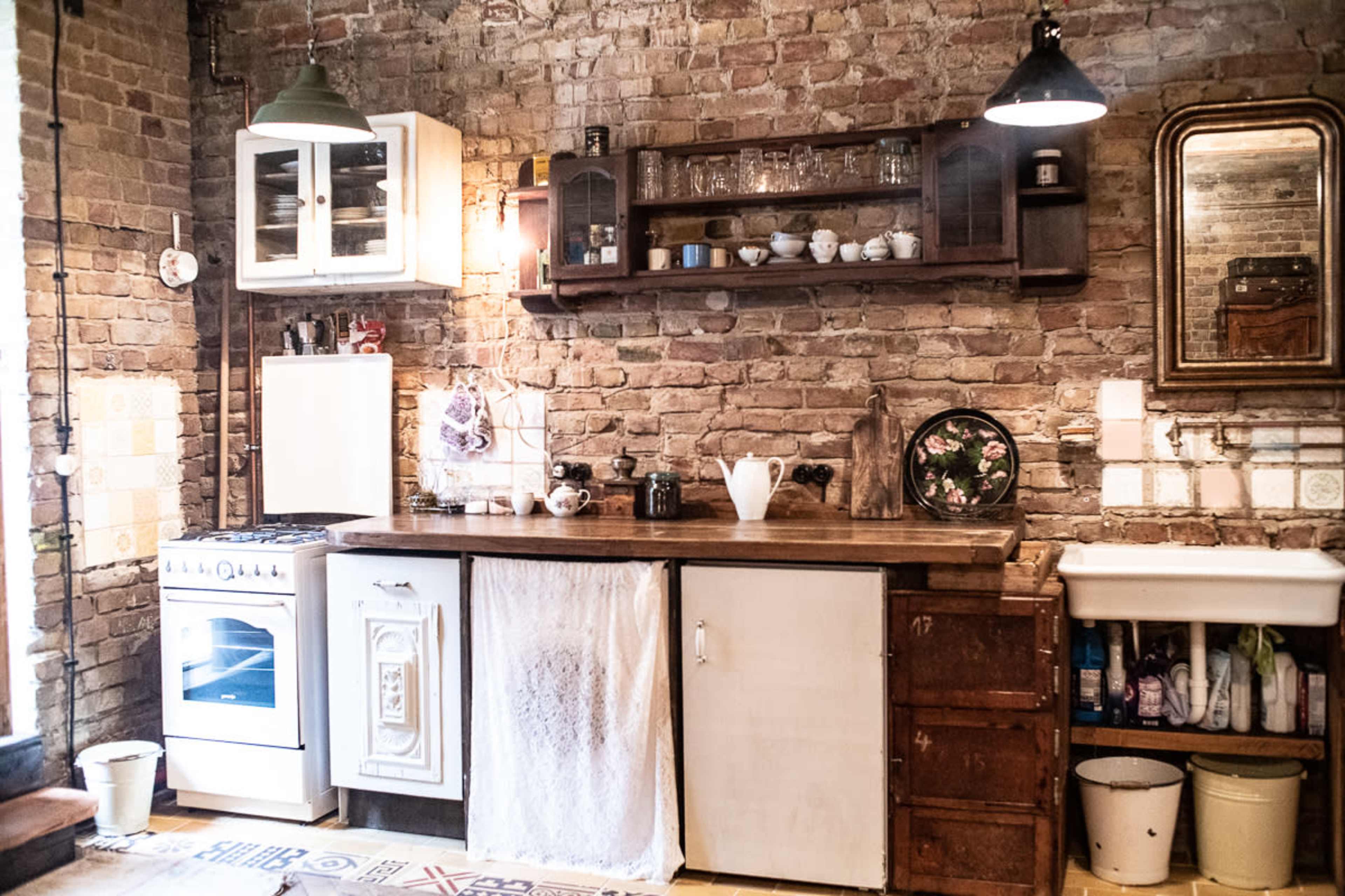 A rustic kitchen features exposed brick walls, a wooden countertop, a white stove, and various dishware displayed on shelves.