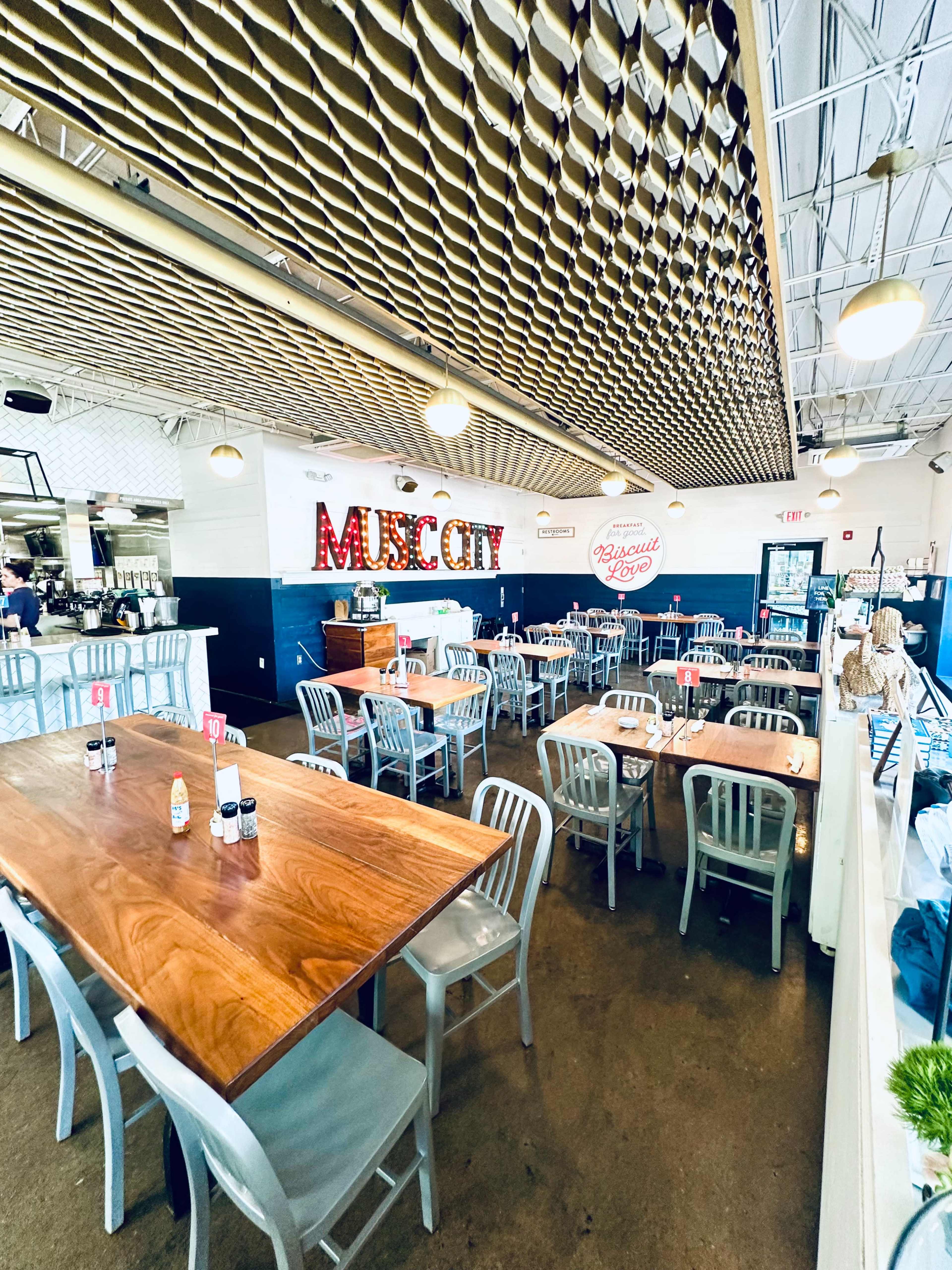 A spacious restaurant interior features wooden tables and metal chairs, with decorative signage that reads "MUSE CITY" on the wall.