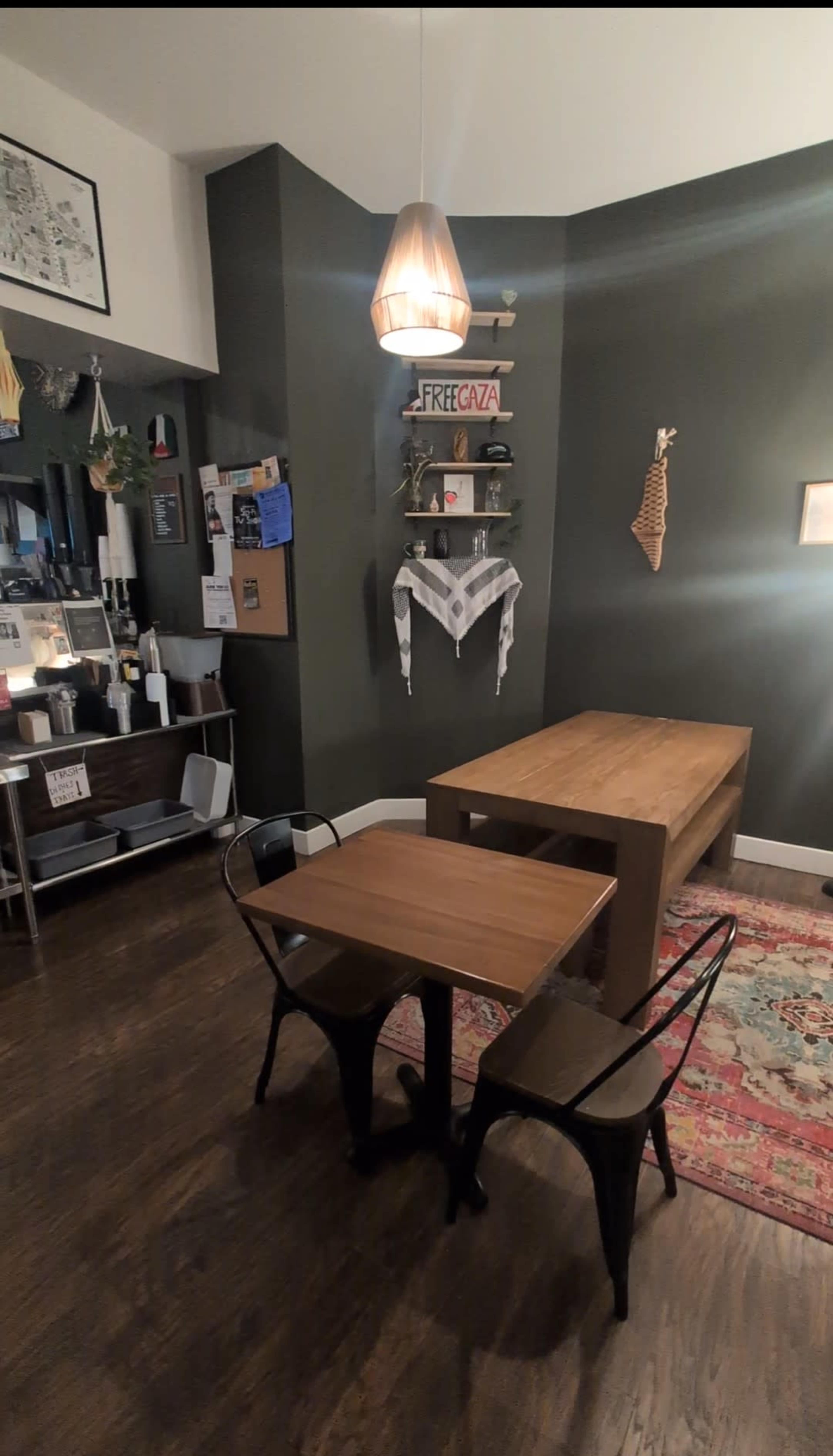The image shows a cozy dining area with a wooden table, two black chairs, a decorative wall shelf, and a rug on the hardwood floor.