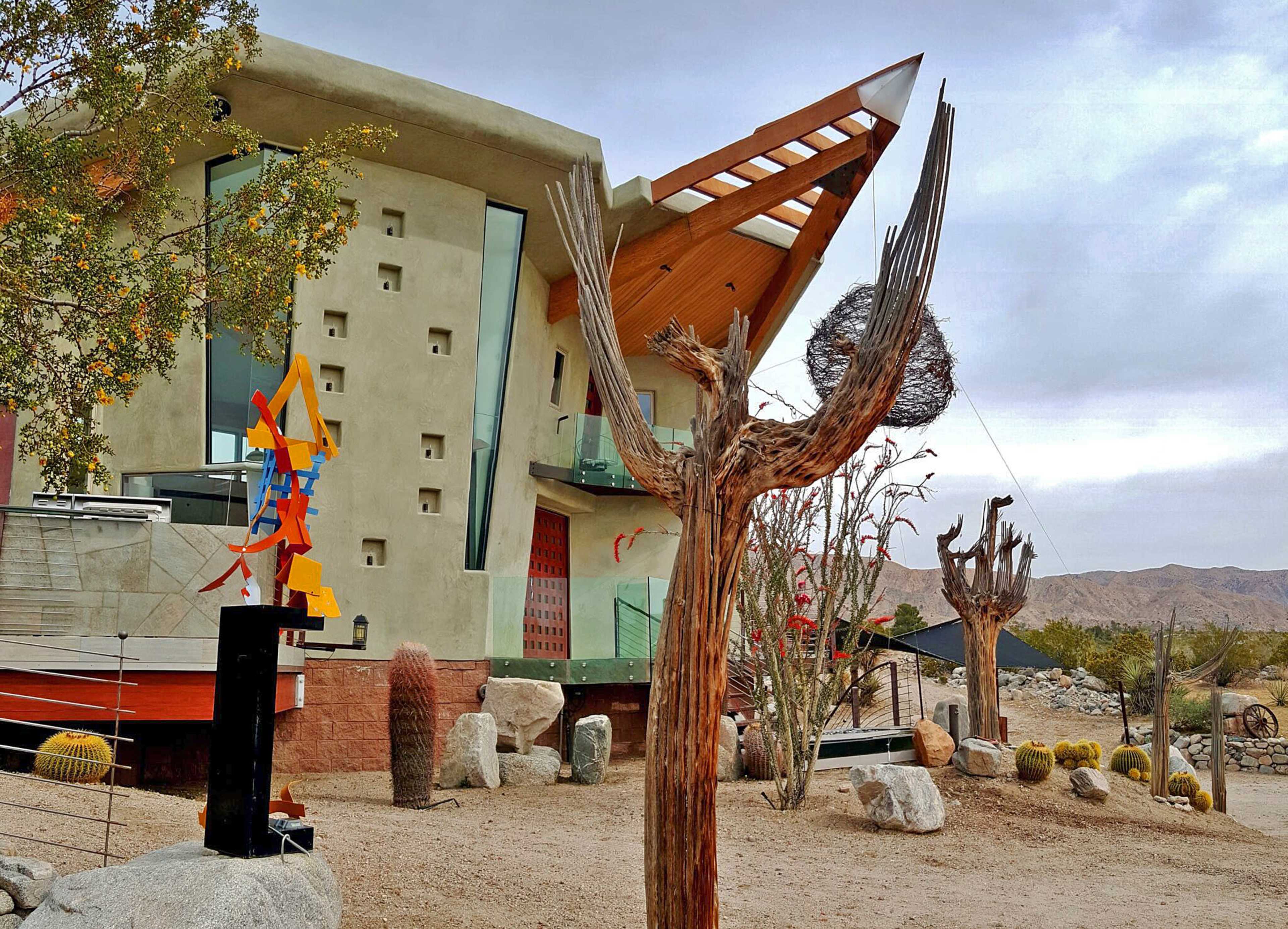 A modern building with an angular design surrounded by desert landscaping, including unique sculptures and native plants.
