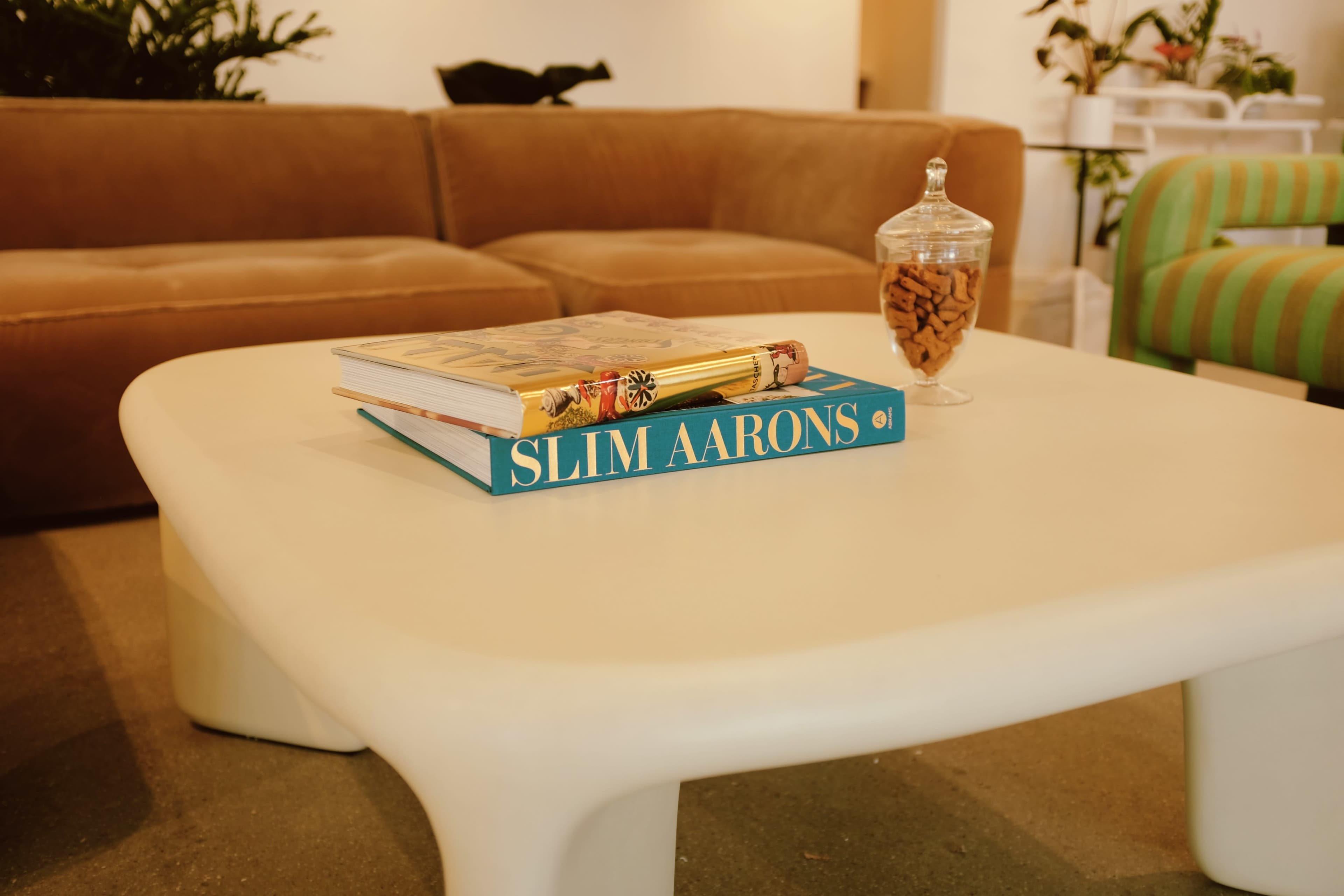 A coffee table features a stack of books and a glass jar filled with snacks in a cozy seating area.