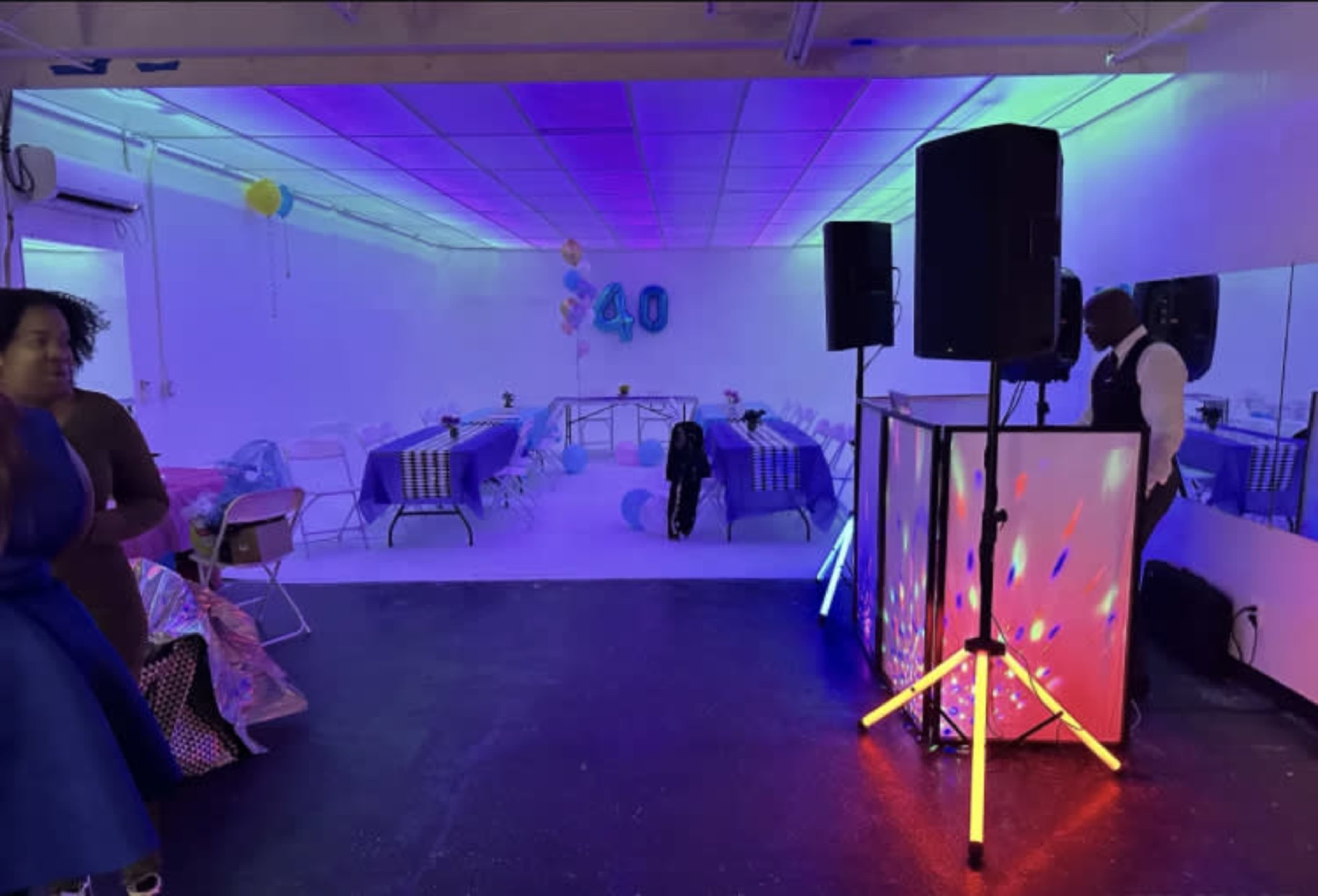 A brightly lit event space features tables with blue and silver decorations, a DJ setup, and a large "40" sign in the background.