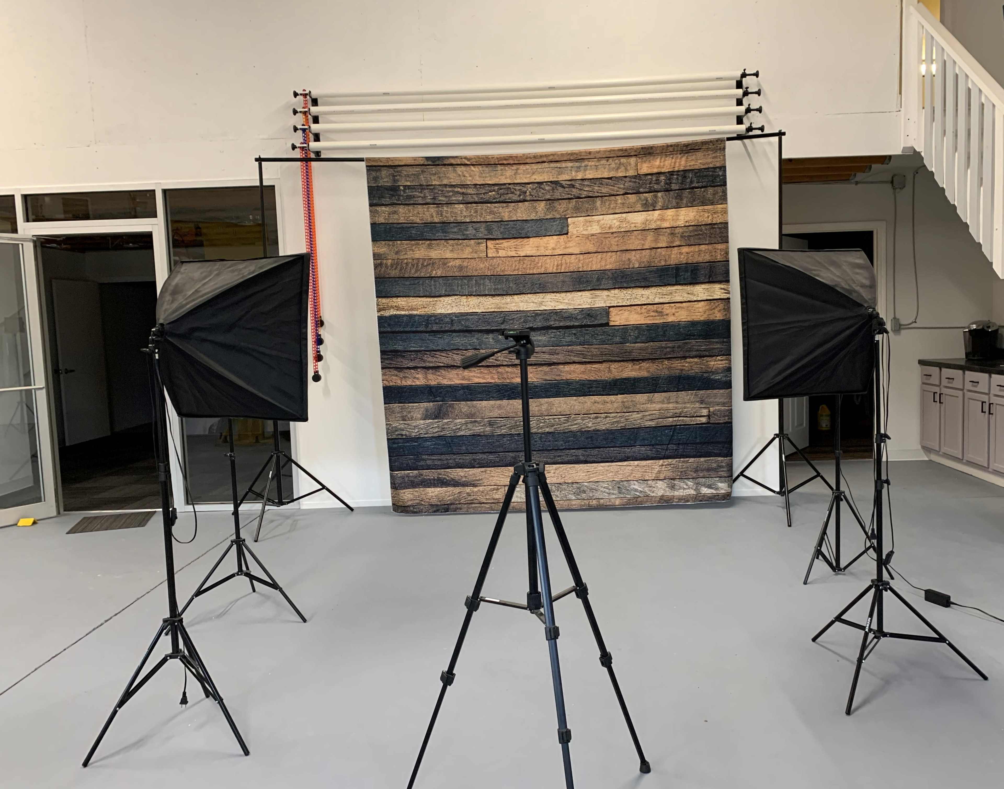 A photography studio setup with two softbox lights and a tripod facing a striped backdrop made of wood planks.