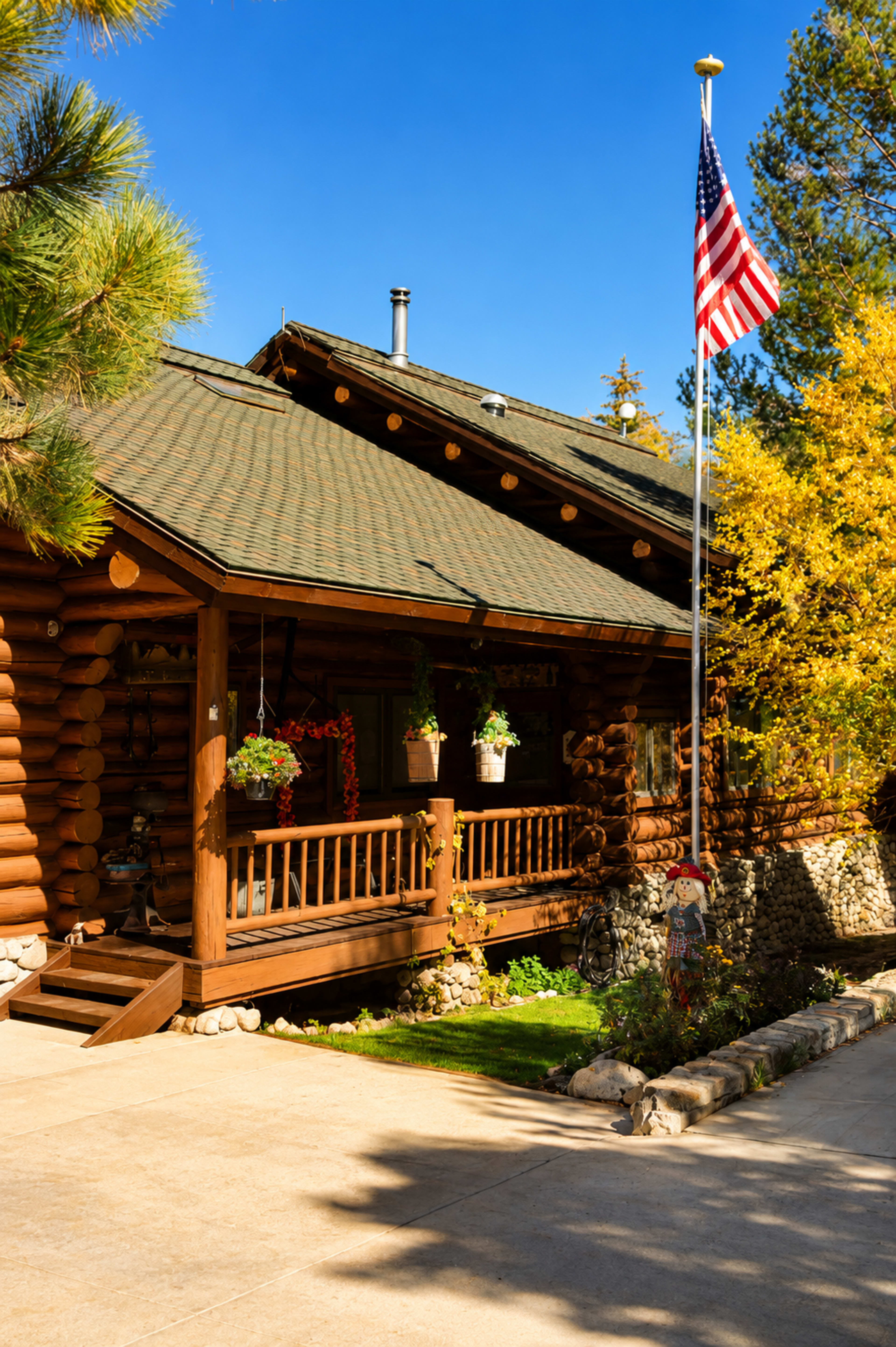 A log cabin with a flagpole displaying the American flag stands amidst autumn foliage and a well-kept garden.