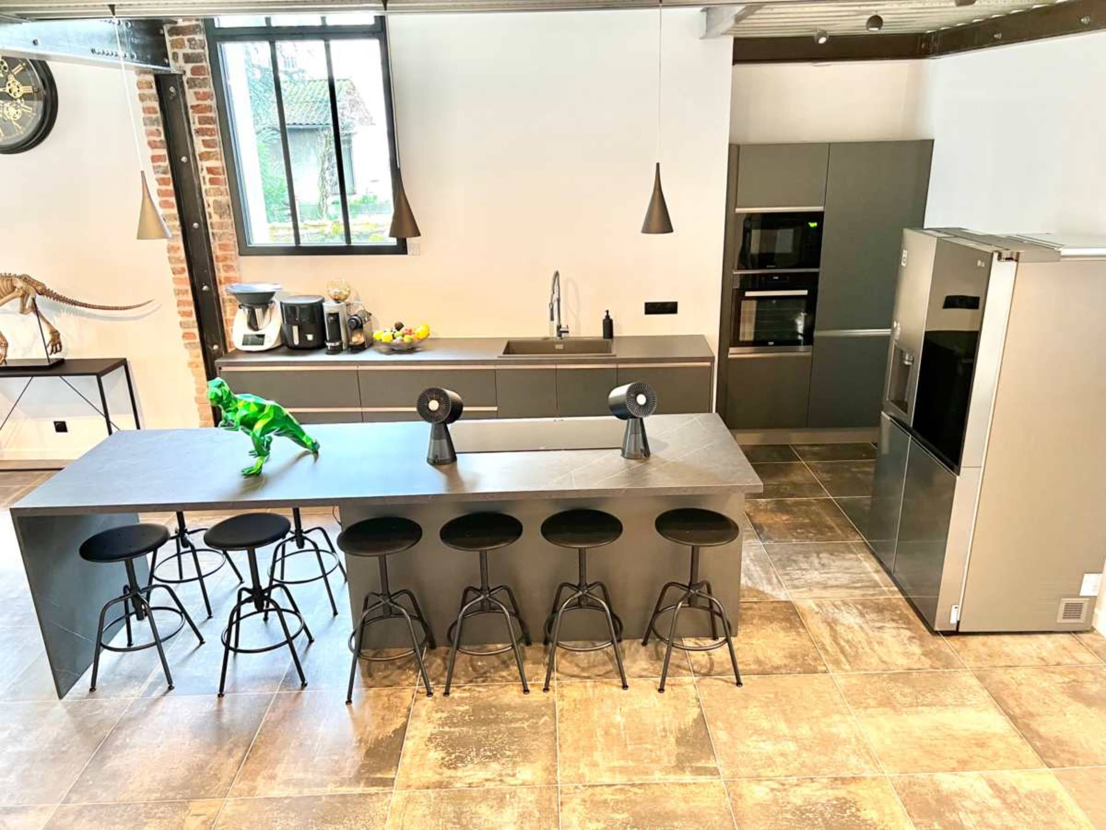 A modern kitchen with gray cabinetry, a central island with black stools, and stainless steel appliances.