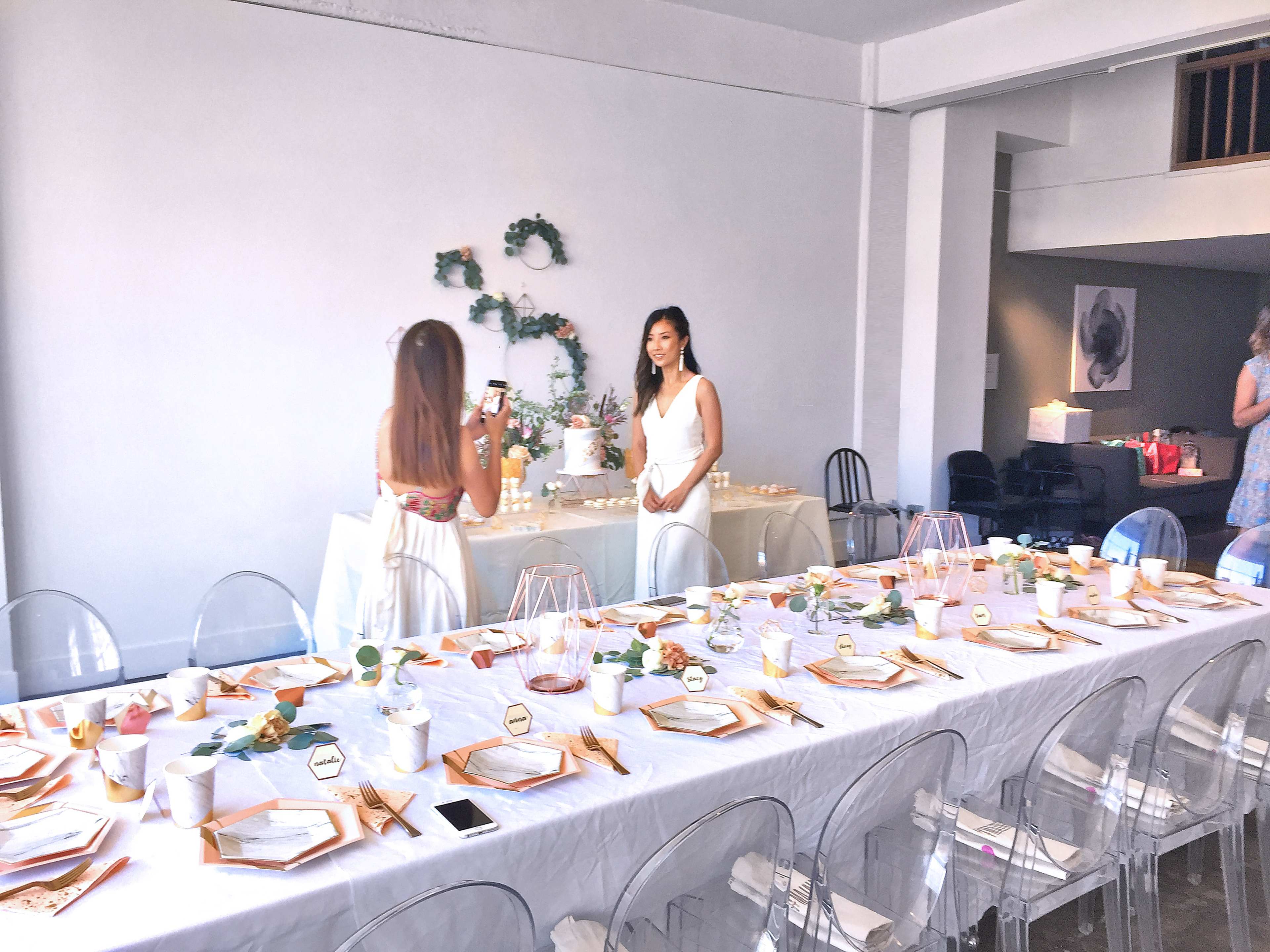 A long dining table is set with place settings and decorations, while two women pose for a photo in a bright, spacious room.