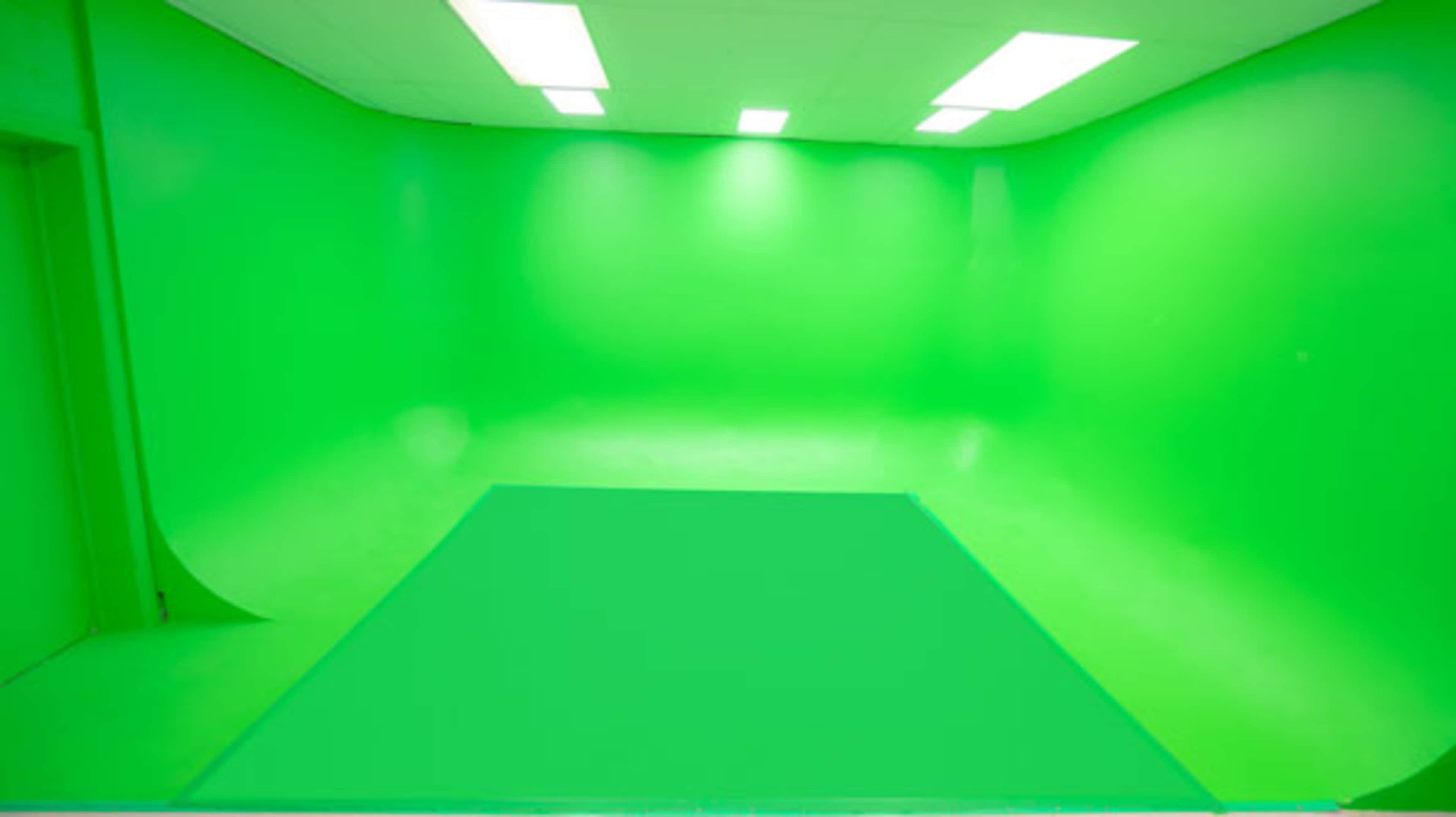 The image shows an empty green screen studio with a seamless green backdrop and overhead lighting.