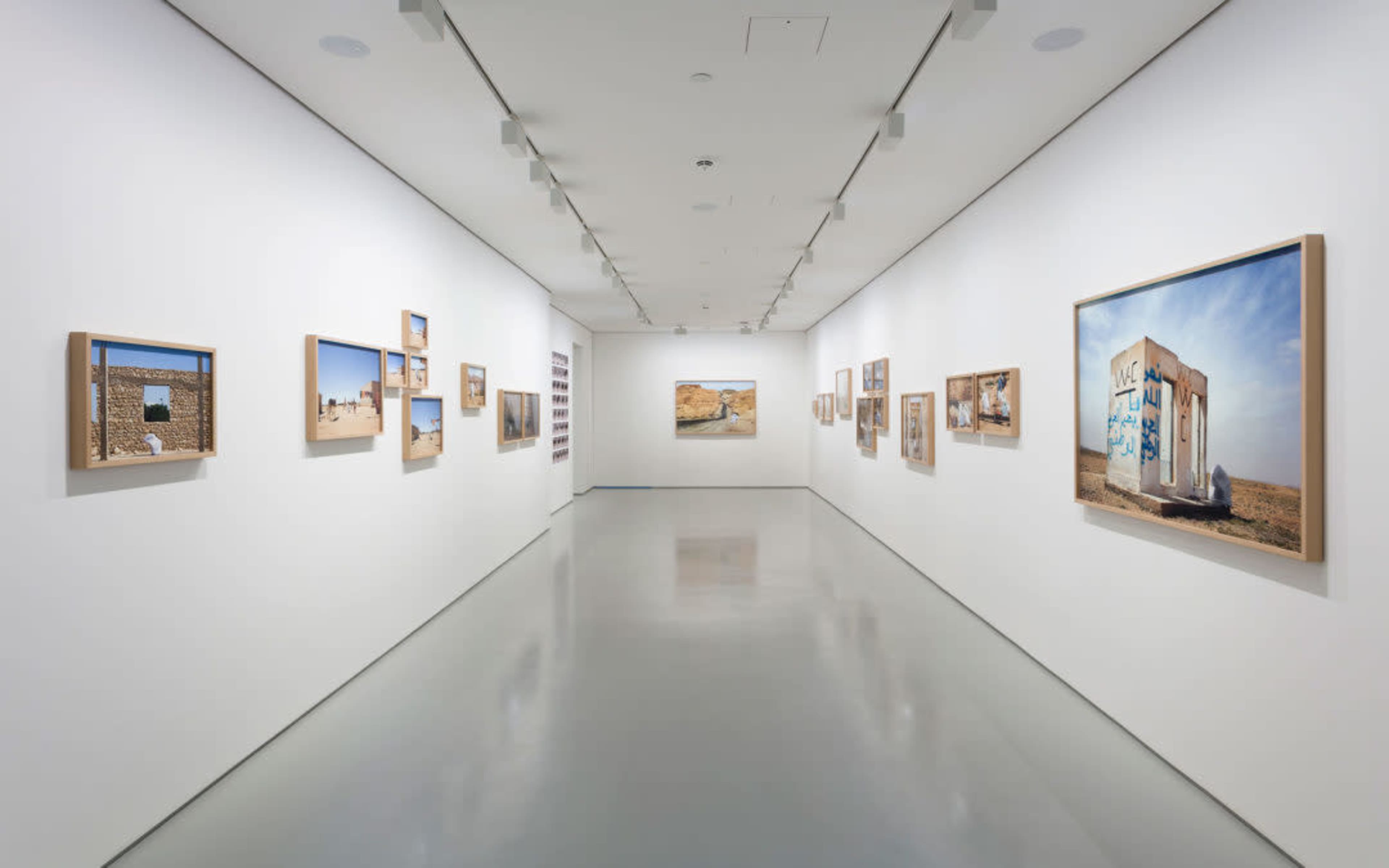 The image shows an art gallery with white walls displaying various framed photographs.