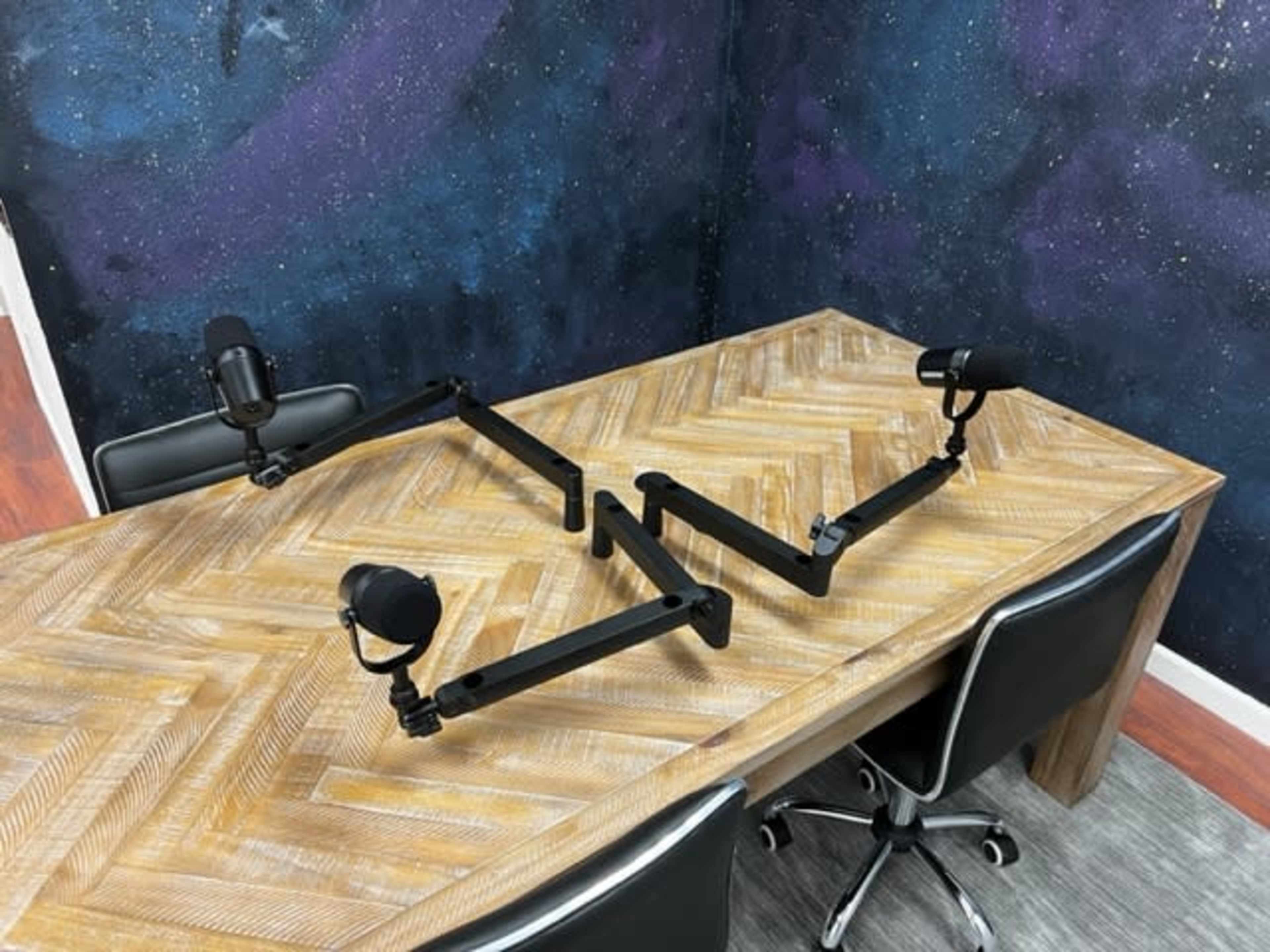 A wooden table with a chevron pattern is equipped with two adjustable microphone arms positioned on opposite sides.