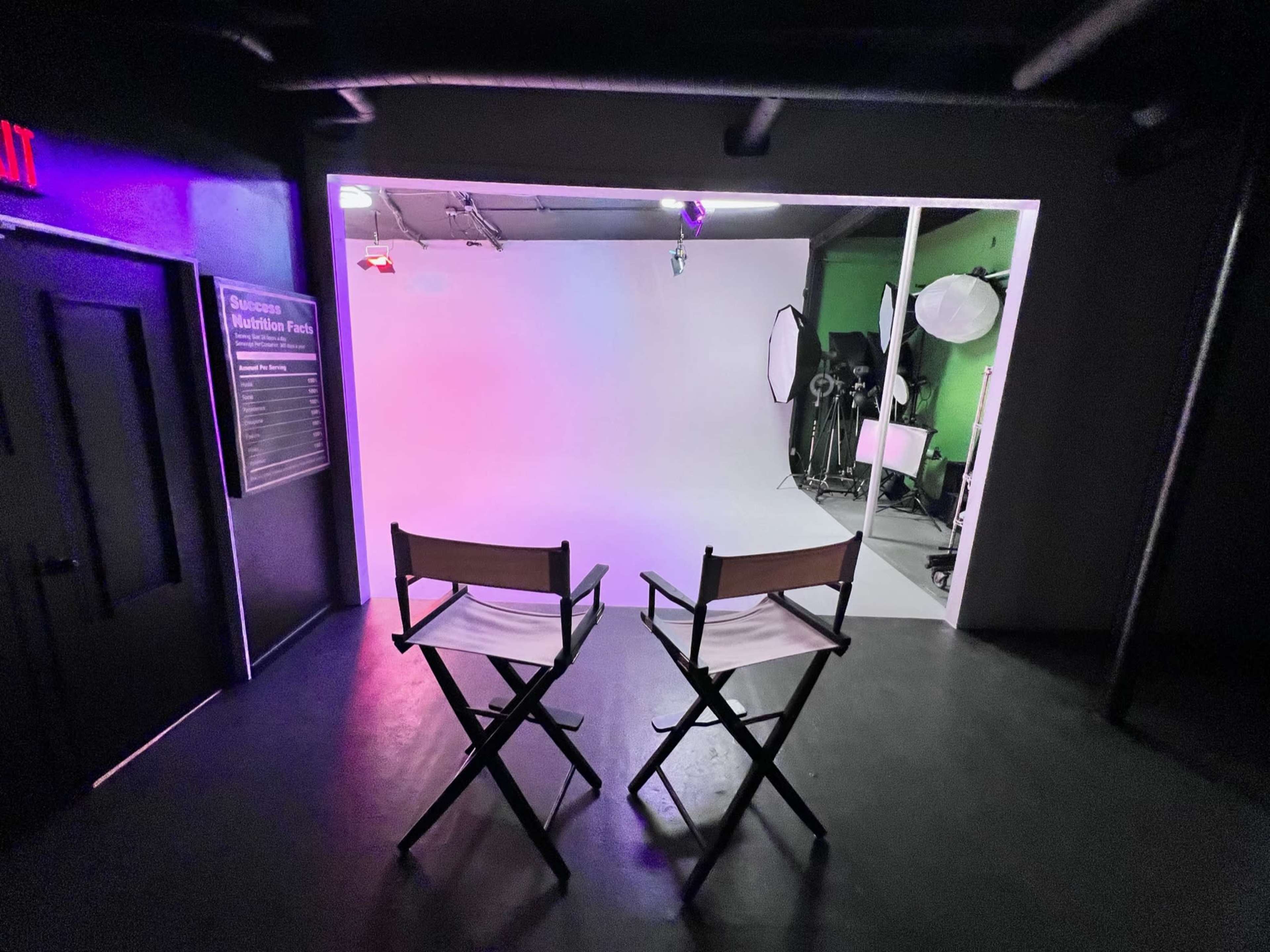 Two empty director's chairs facing a brightly lit photography studio with a white backdrop and various lighting equipment.