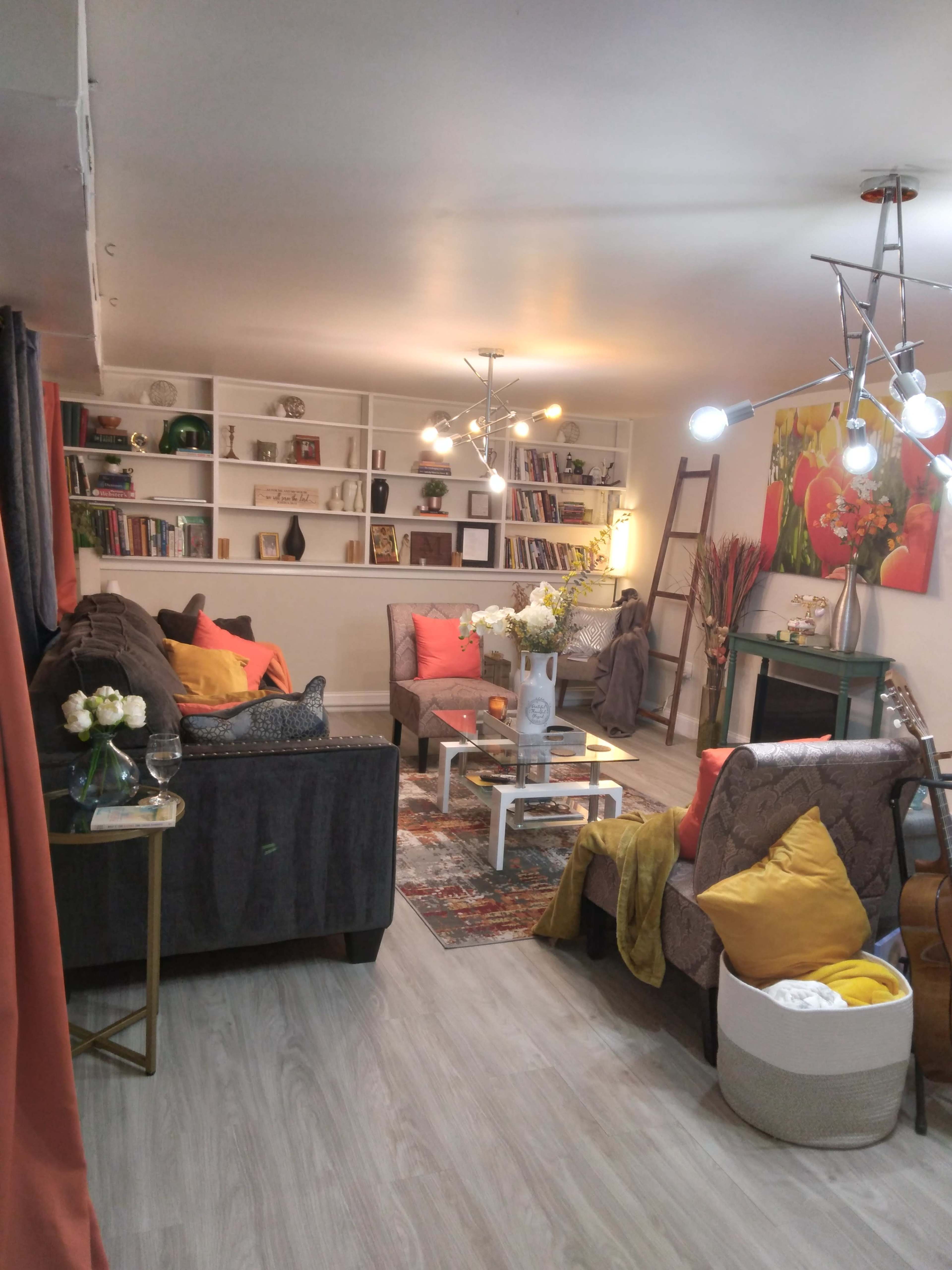 A cozy living room with two sofas, a coffee table, bookshelves, and decorative items, illuminated by a modern light fixture.