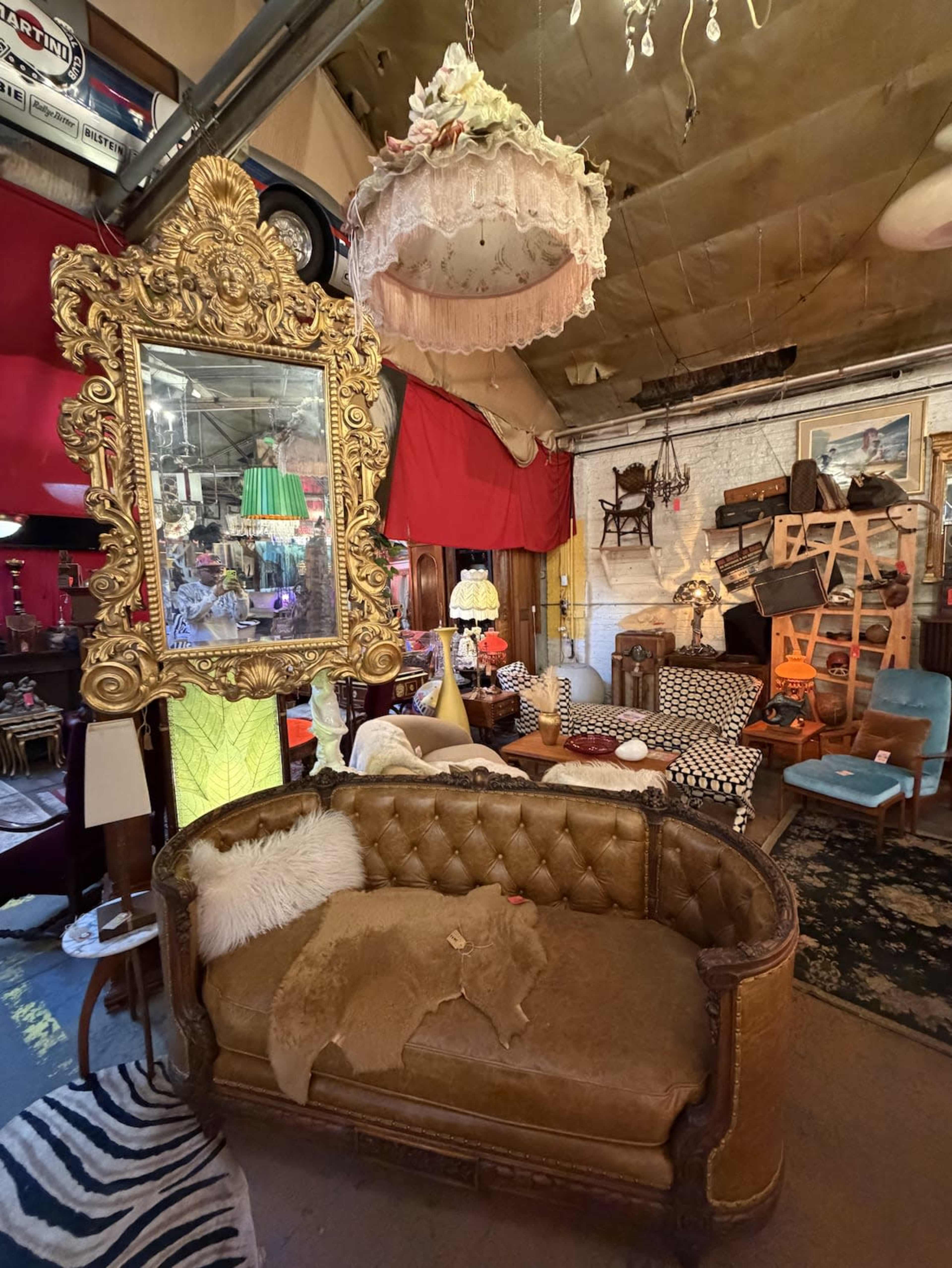 The image shows a vintage-style shop interior filled with various furniture items, including a tufted couch, ornate mirror, and eclectic light fixtures.