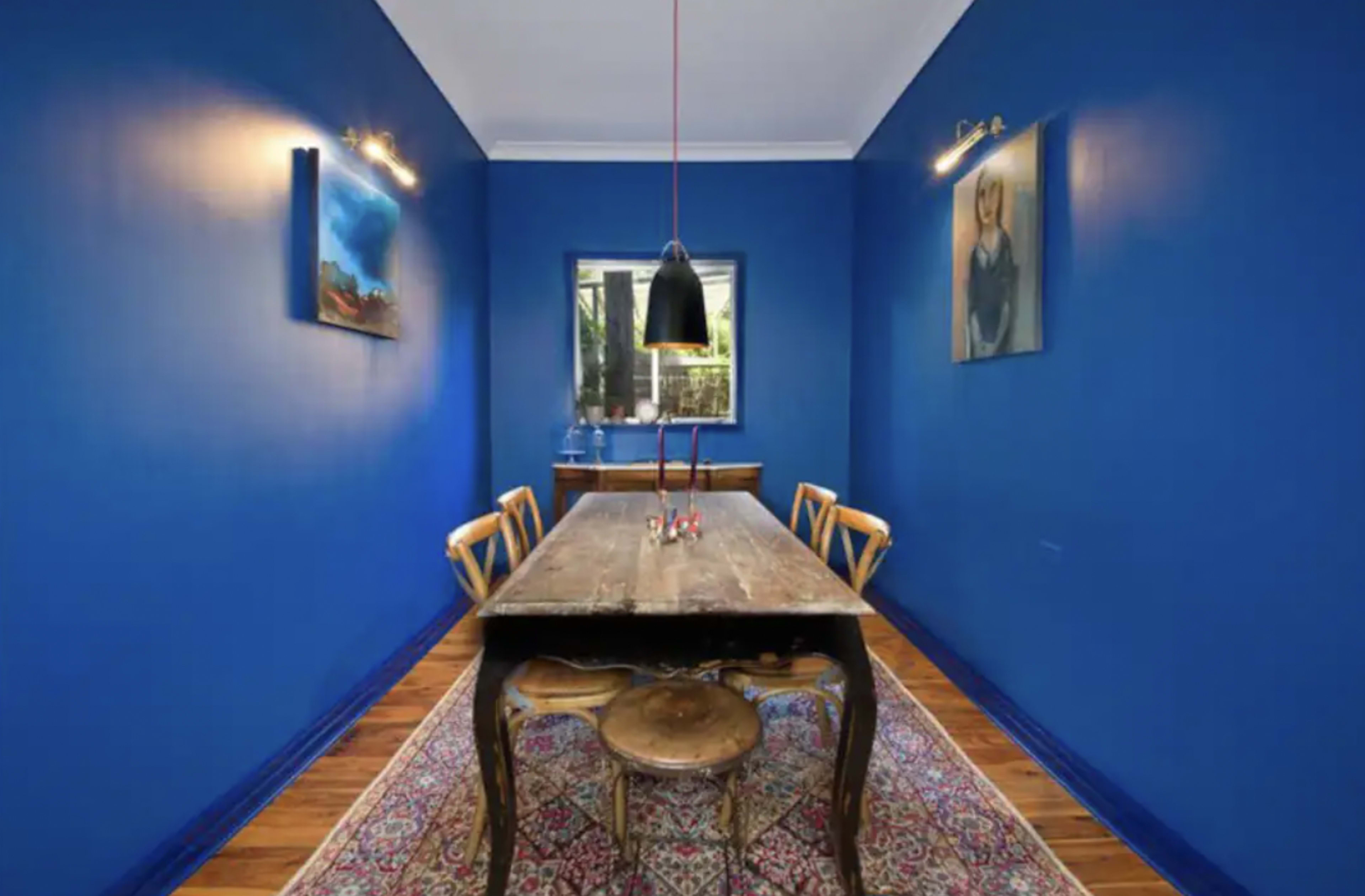 A dining room with blue walls, a wooden table surrounded by chairs, and artwork hanging on the walls.