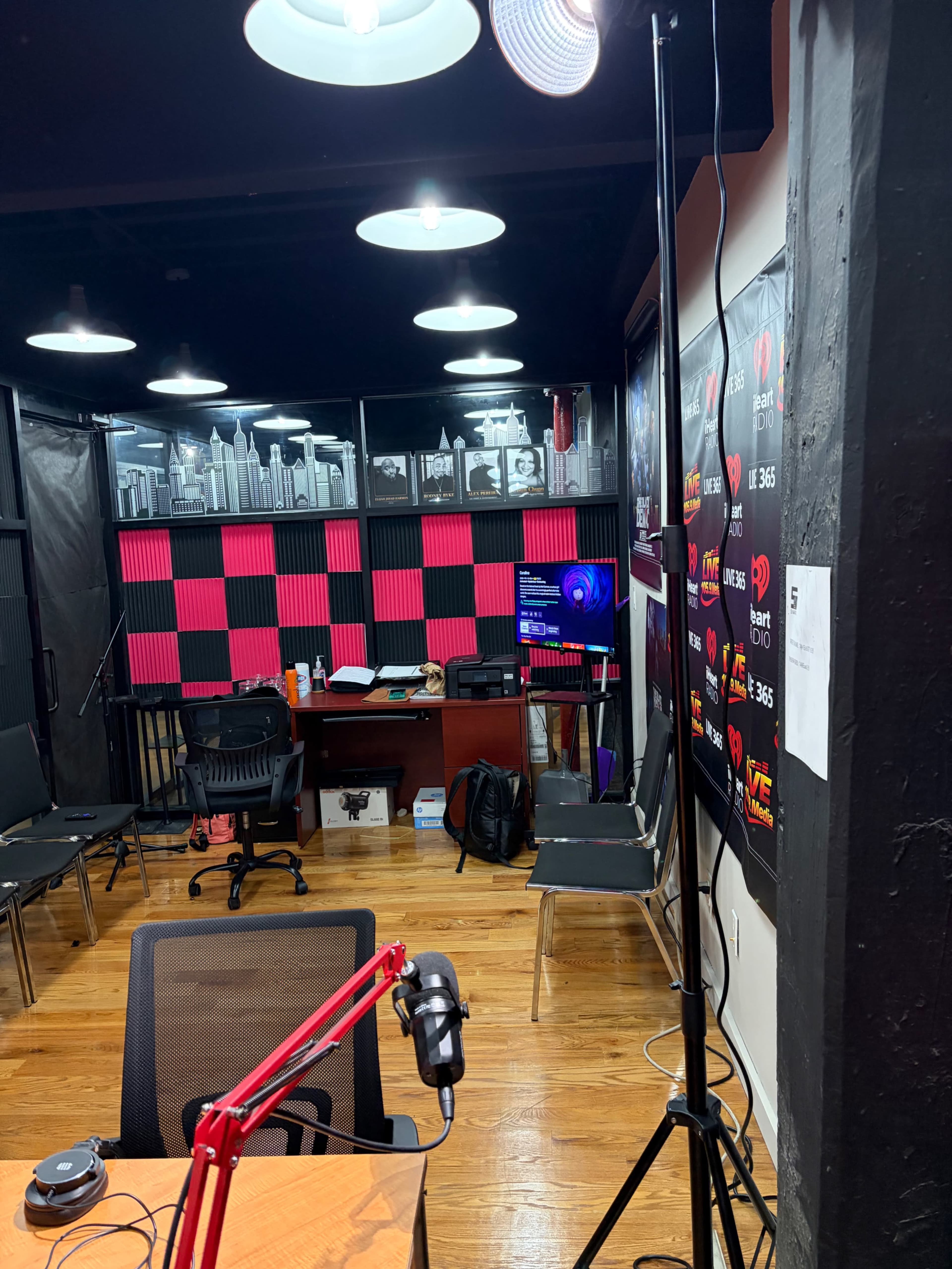 The image shows a recording studio with a checkerboard wall, seating, a desk with equipment, and various lights.