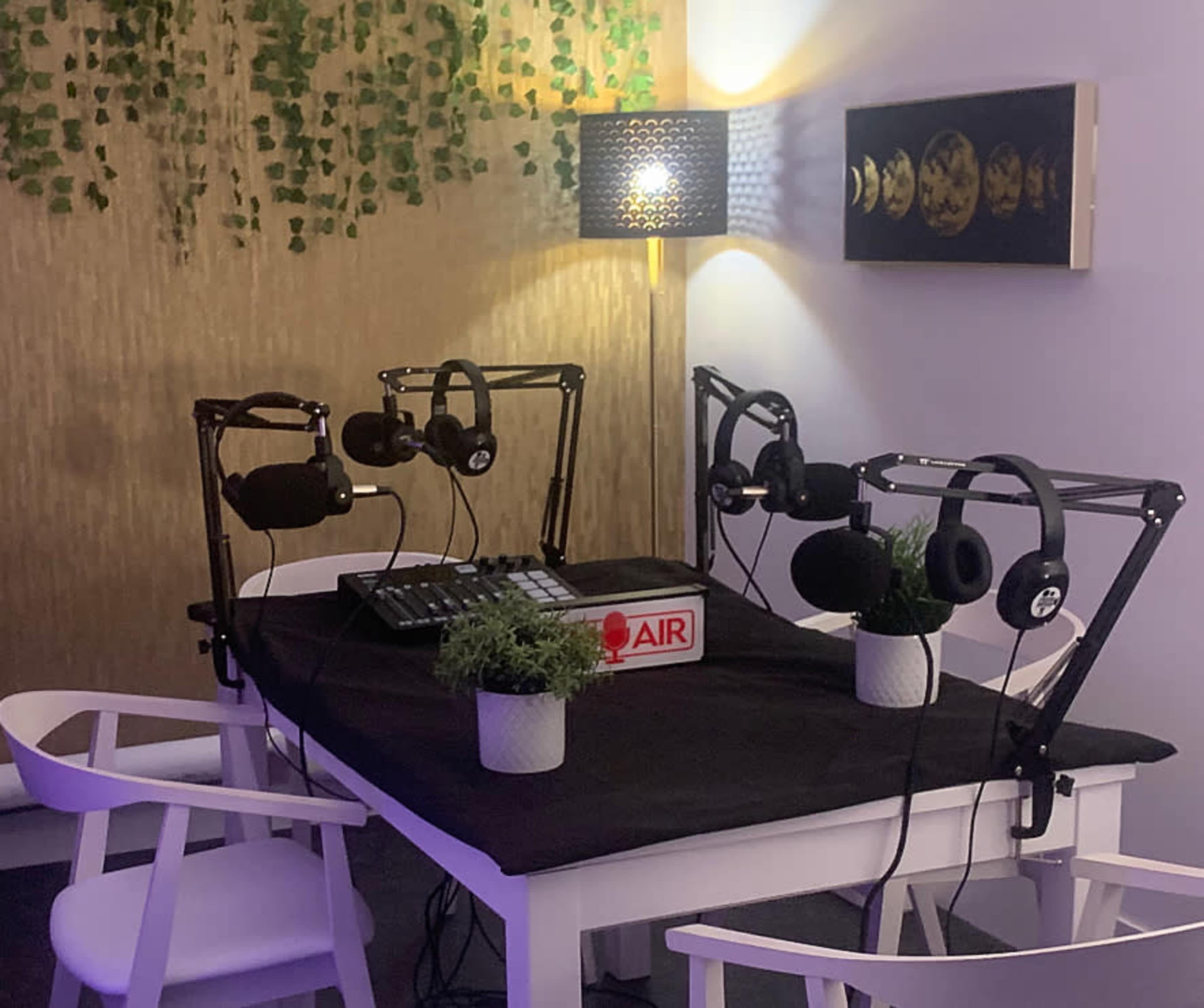 A podcast recording setup featuring a table with microphones, headphones, and a sound mixer, surrounded by decorative plants and soft lighting.