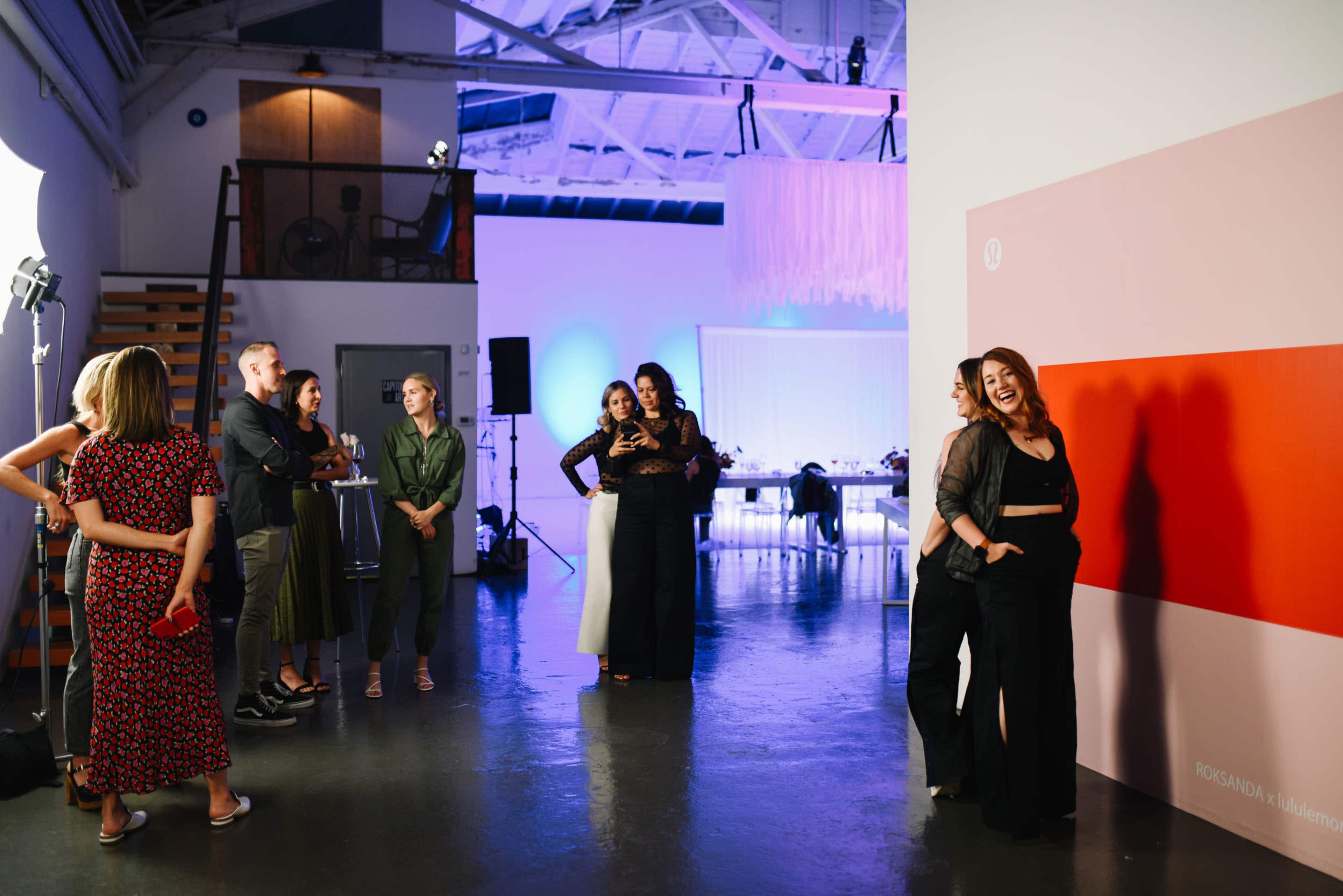 A group of people socializes in a modern event space featuring a large wall with a simple color design and dim, ambient lighting.