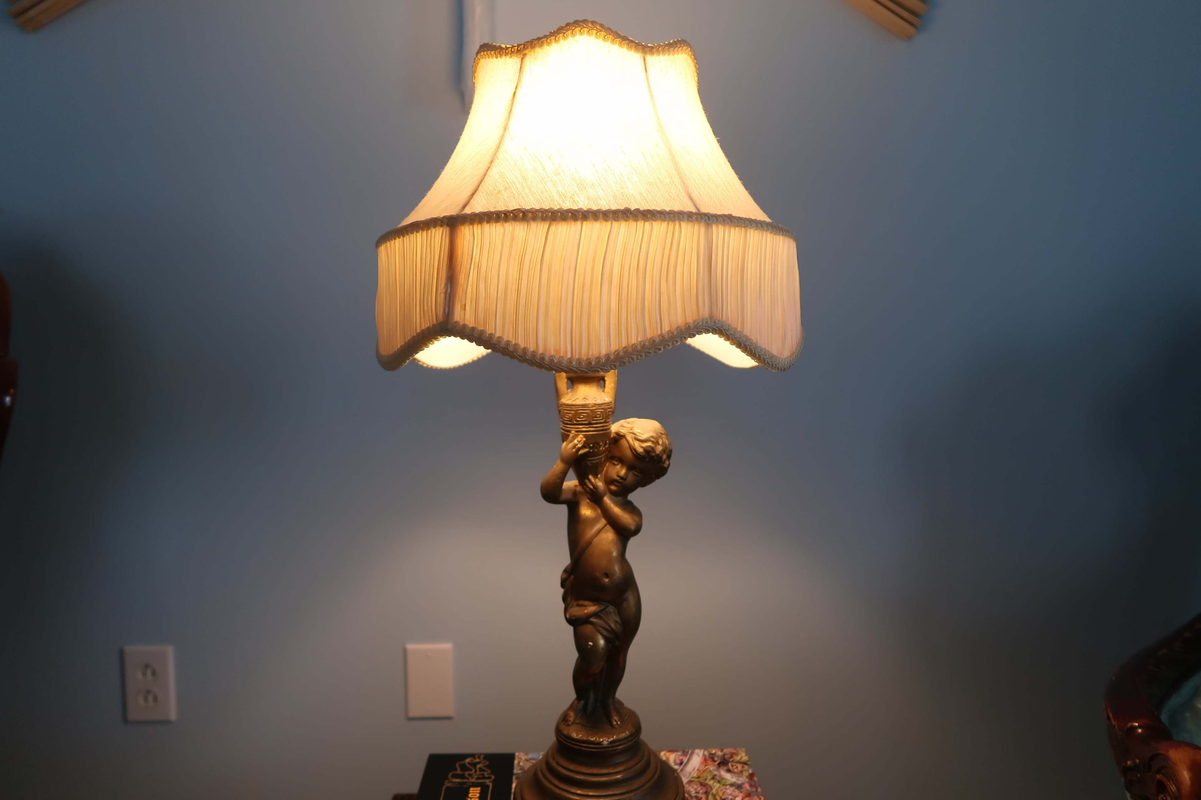 A decorative lamp featuring a child figurine as the base and a beige lampshade.