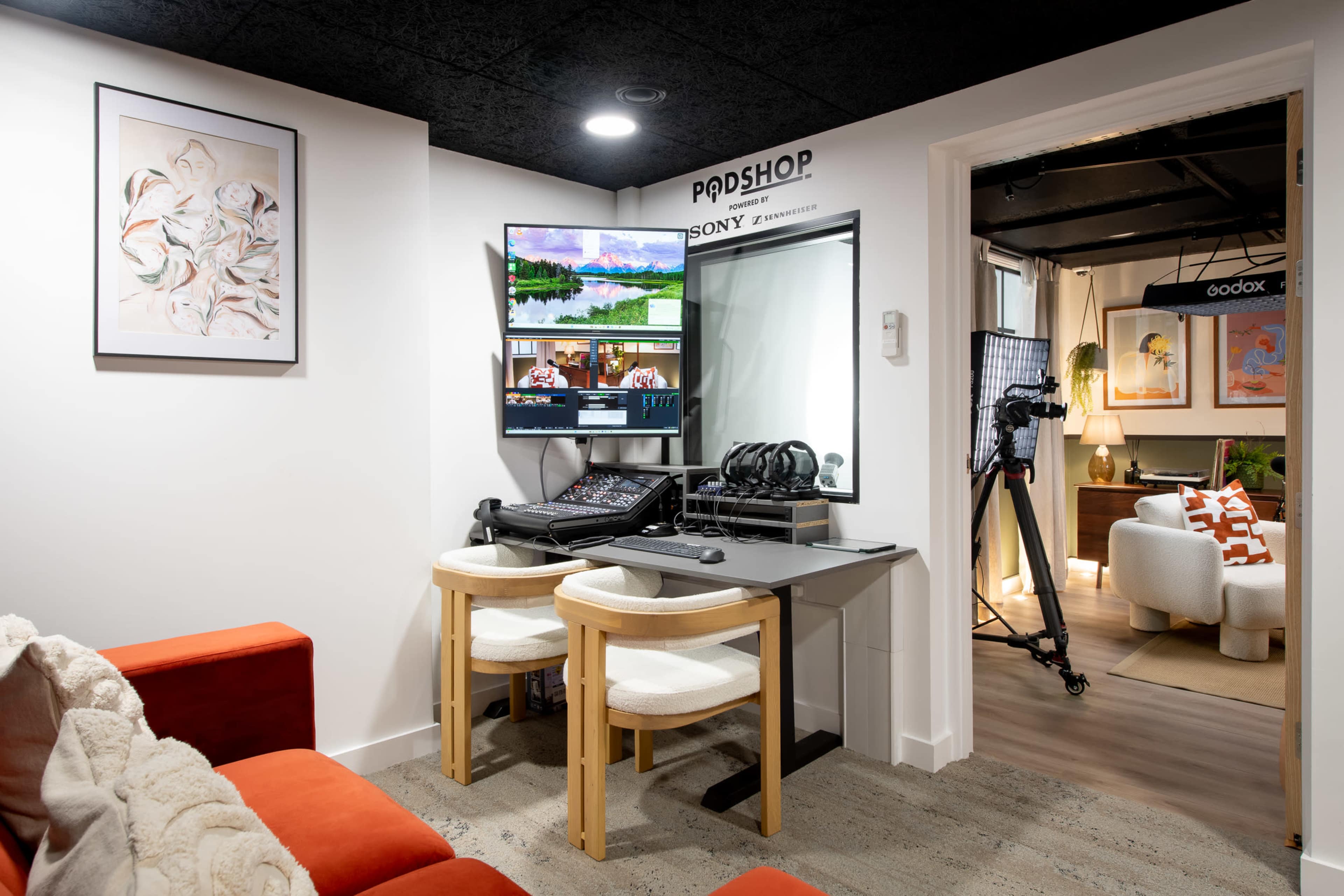 The image shows a modern workspace featuring a desk with multiple monitors, audio equipment, and a comfortable seating area in a well-lit room.