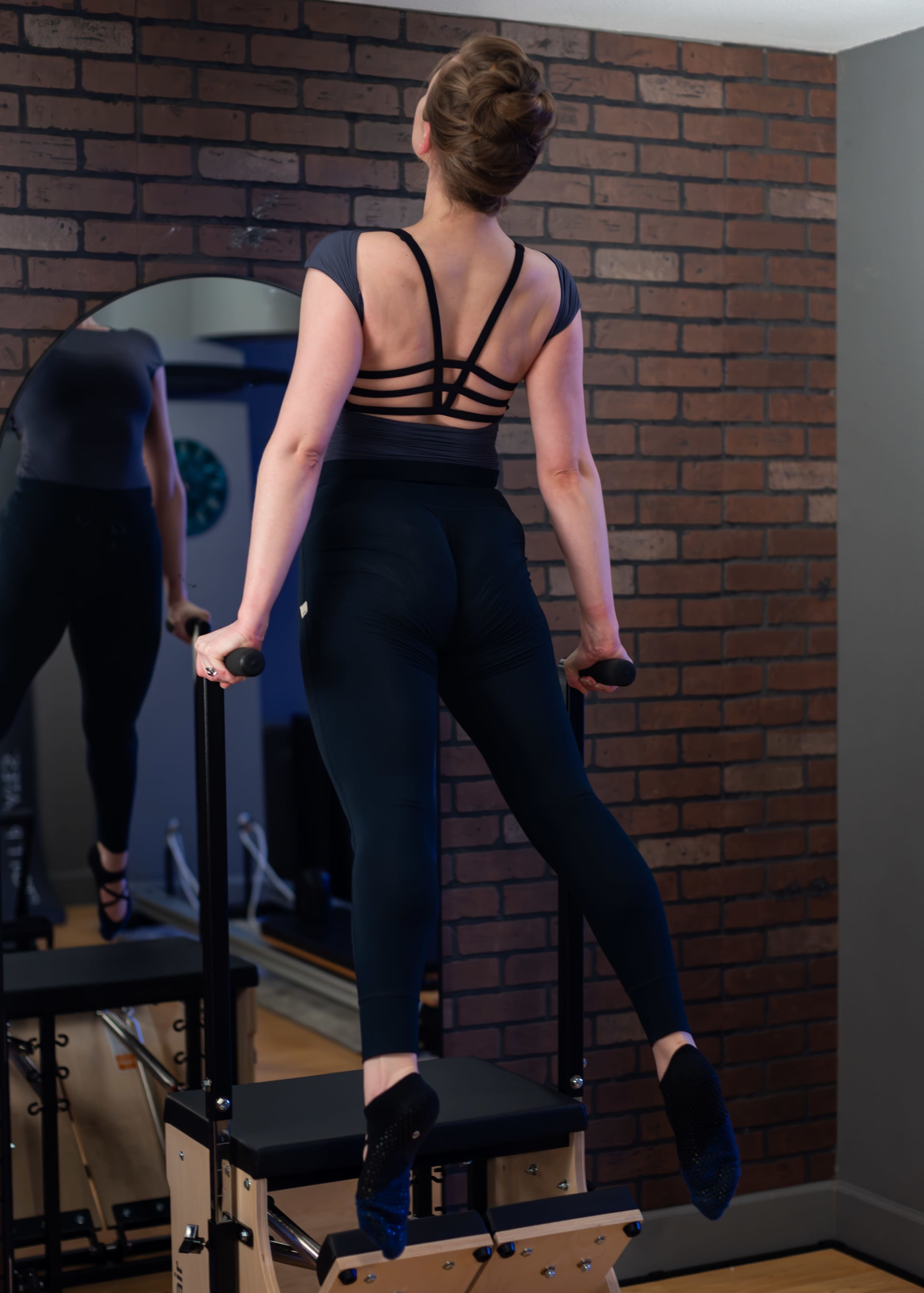 A person performs a pull-up on a fitness apparatus in a room with a brick wall and a mirror.