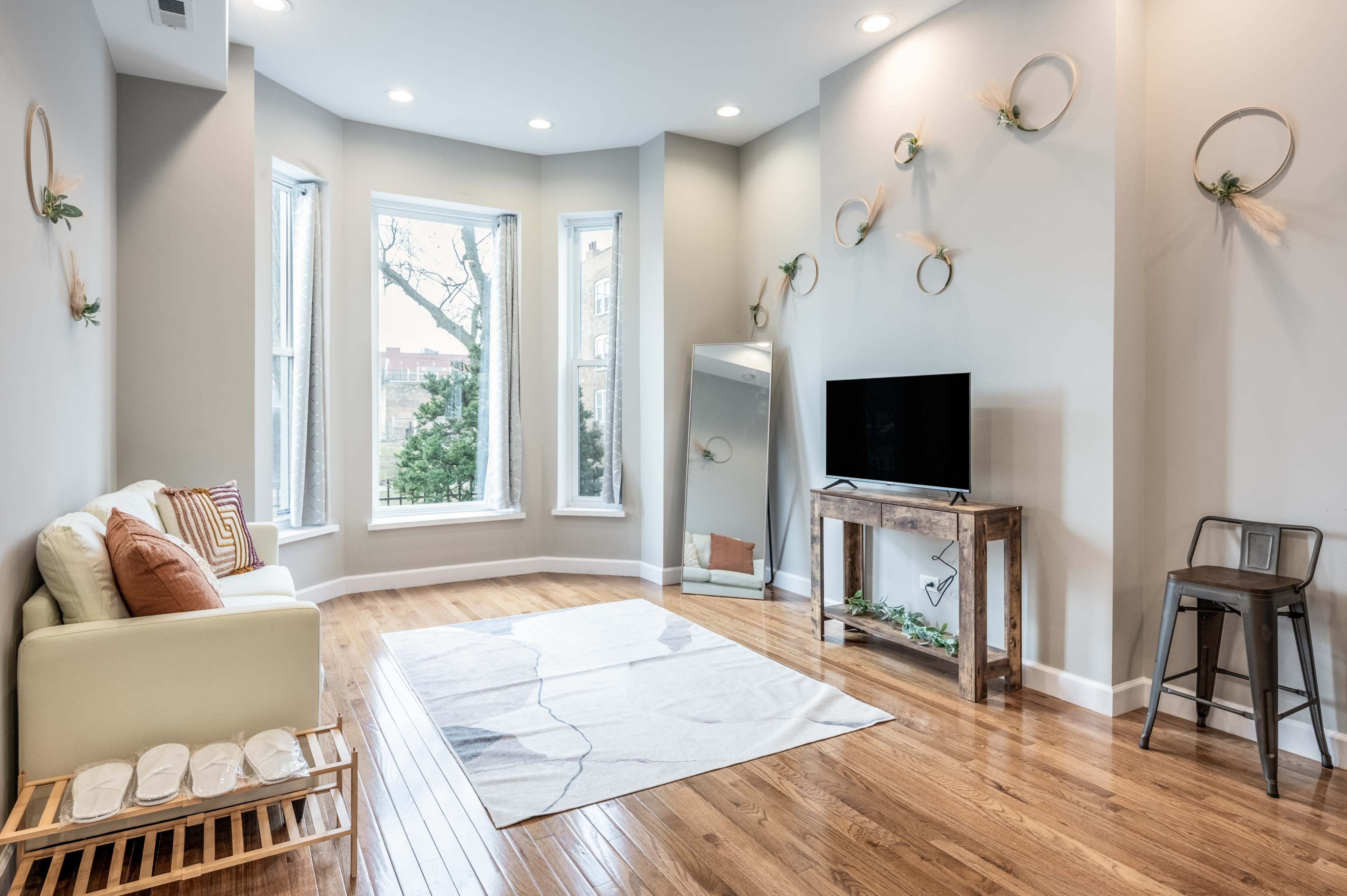 A modern living room features large windows, a sofa, a television on a wooden console, and decorative wall elements.