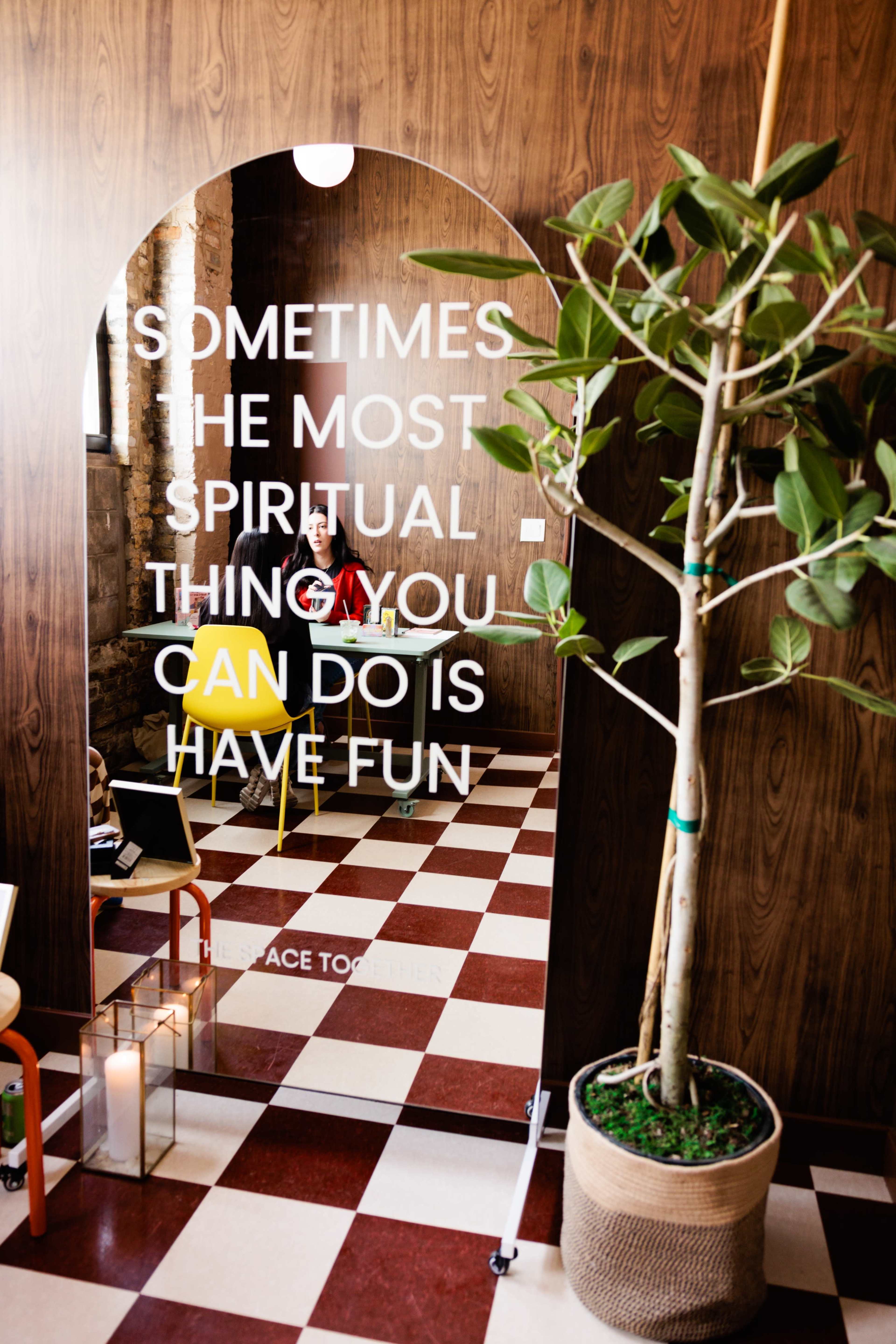 The image shows a stylish interior with a mirrored arch displaying a motivational quote, a potted plant, and checkered flooring.