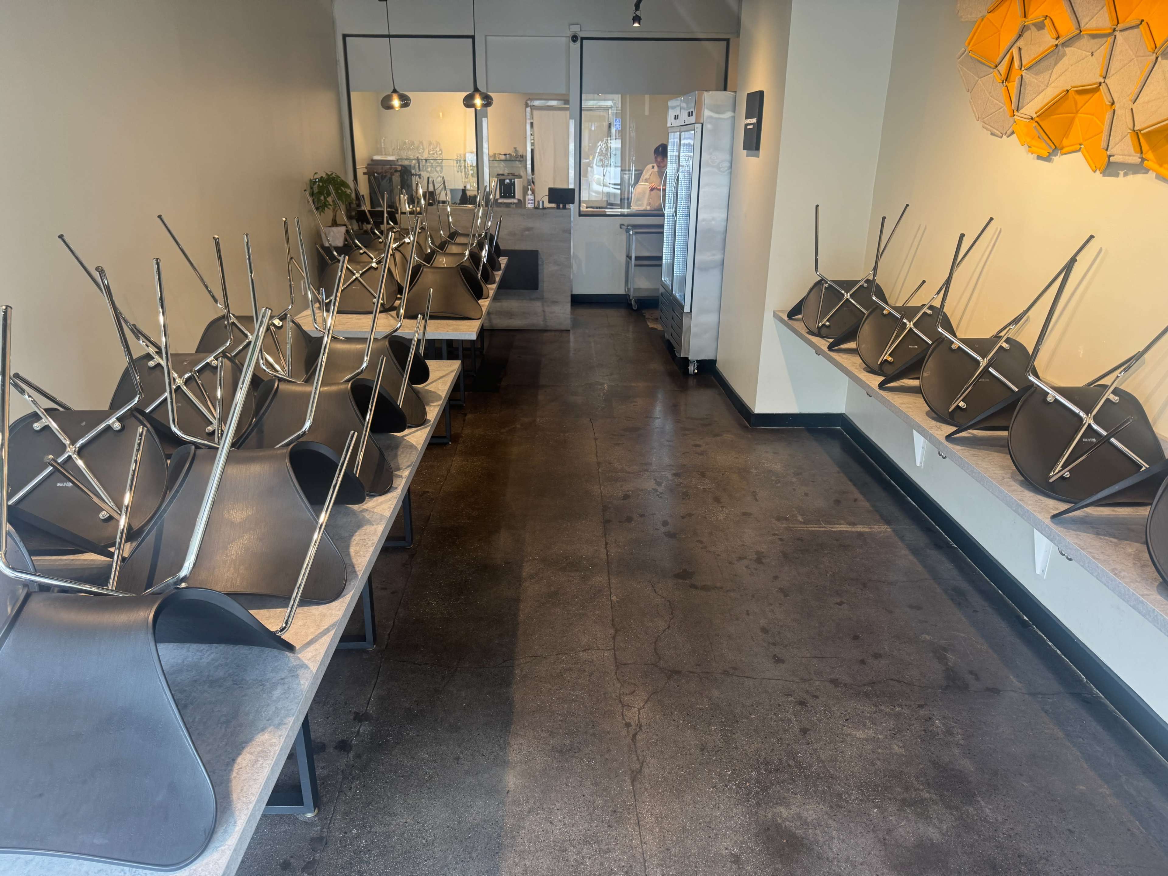 The image shows a mostly empty café with tables turned upside down and stacked chairs resting on the floor.