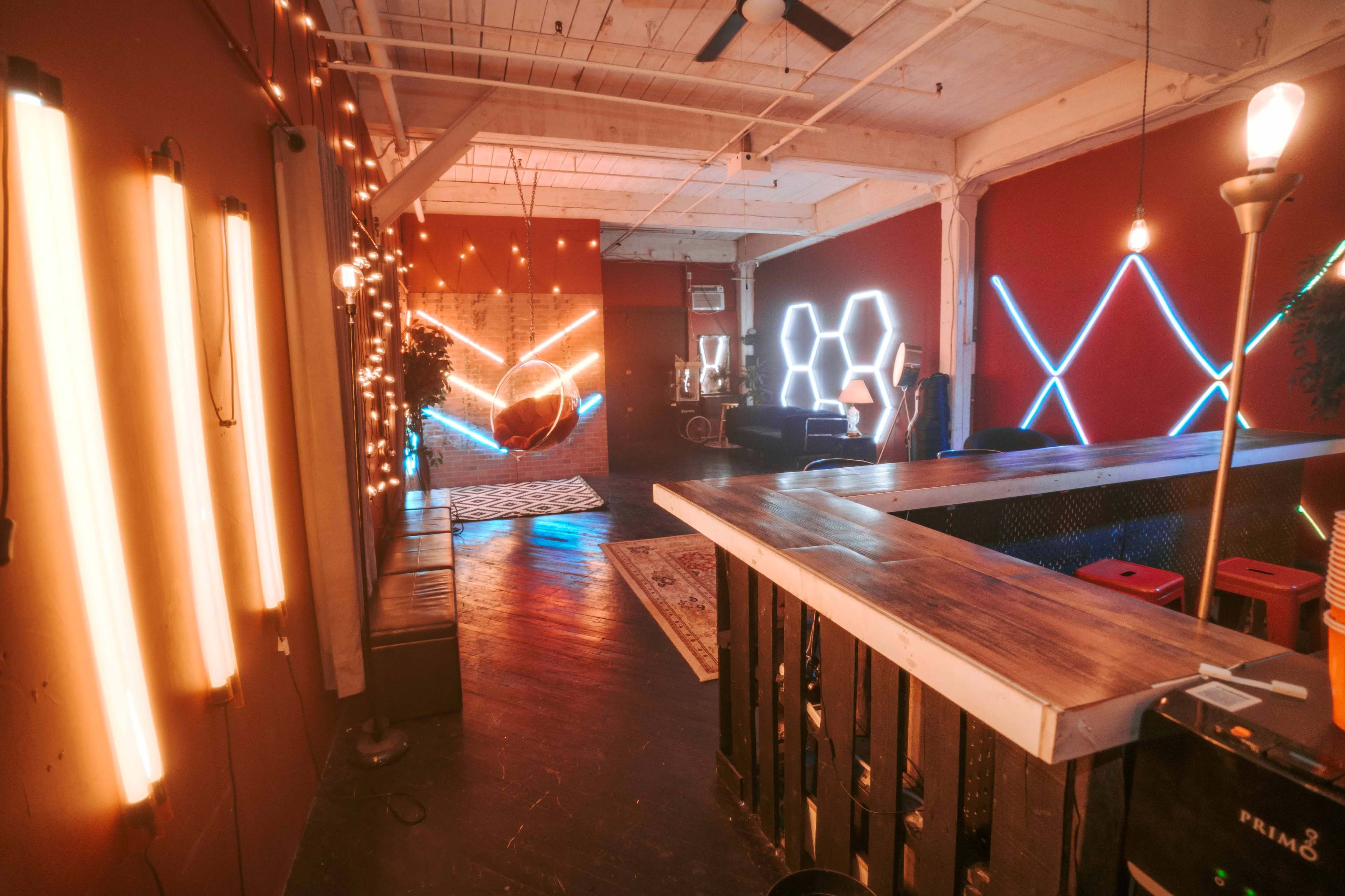 The image shows a modern, stylish interior space featuring a bar area, illuminated wall designs, and a mix of seating options.