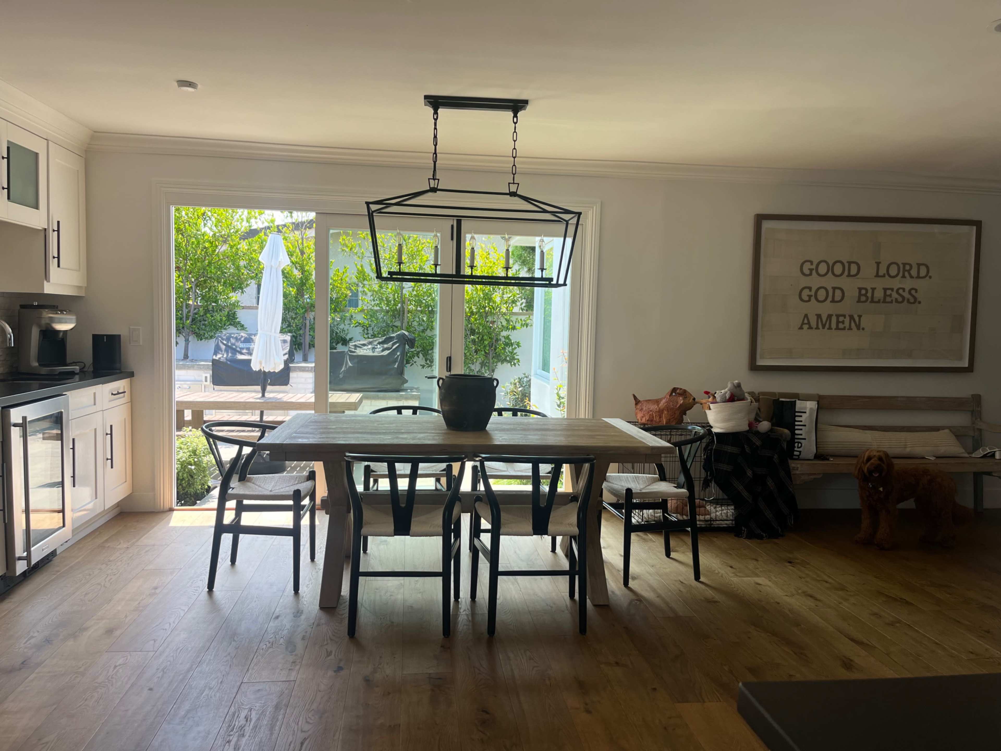 A dining area features a wooden table surrounded by chairs, with a large window overlooking a patio and greenery.