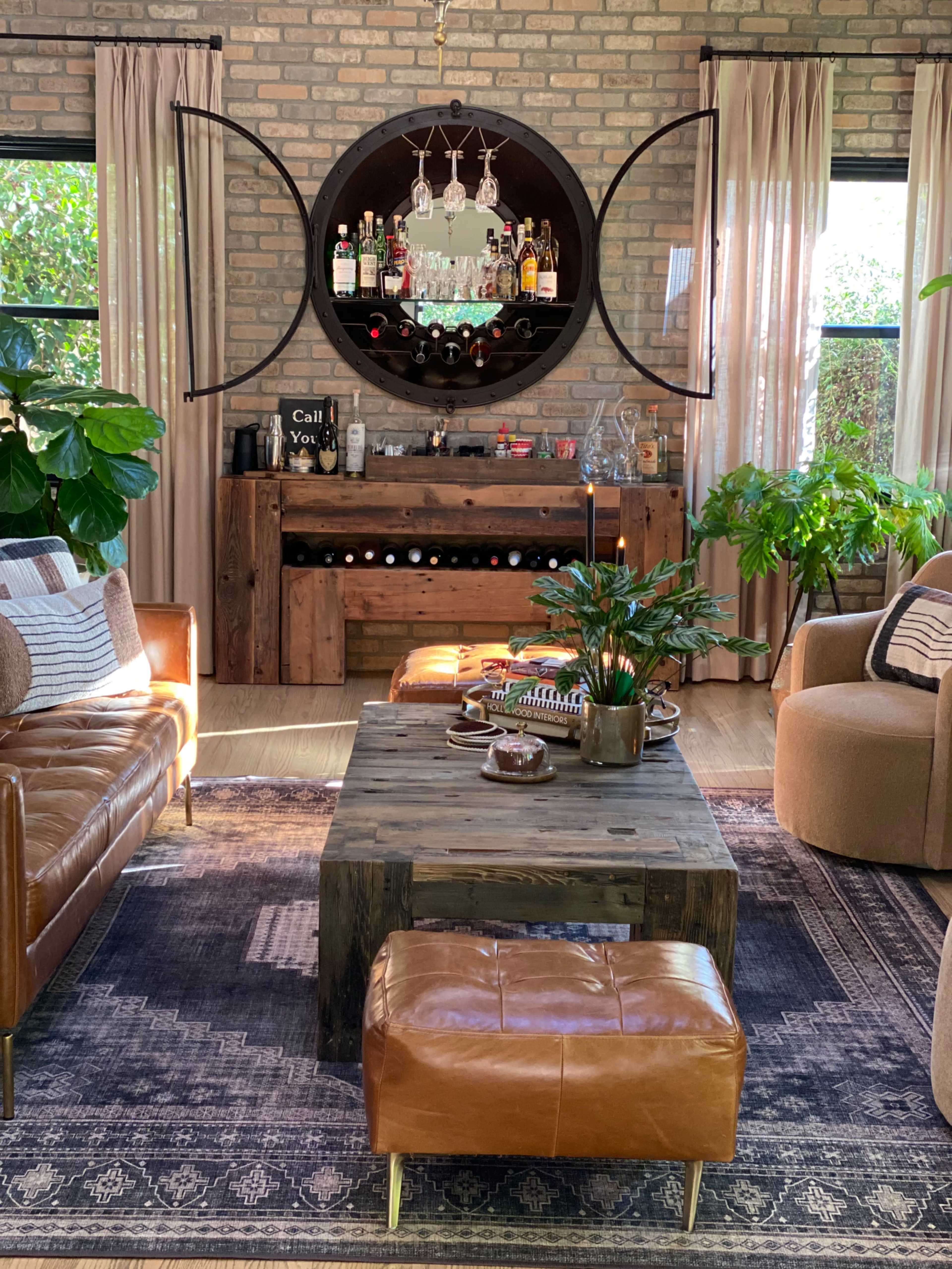 The living room features a rustic wooden coffee table, a circular mirror displaying bottles, and leather seating arranged around a patterned rug.