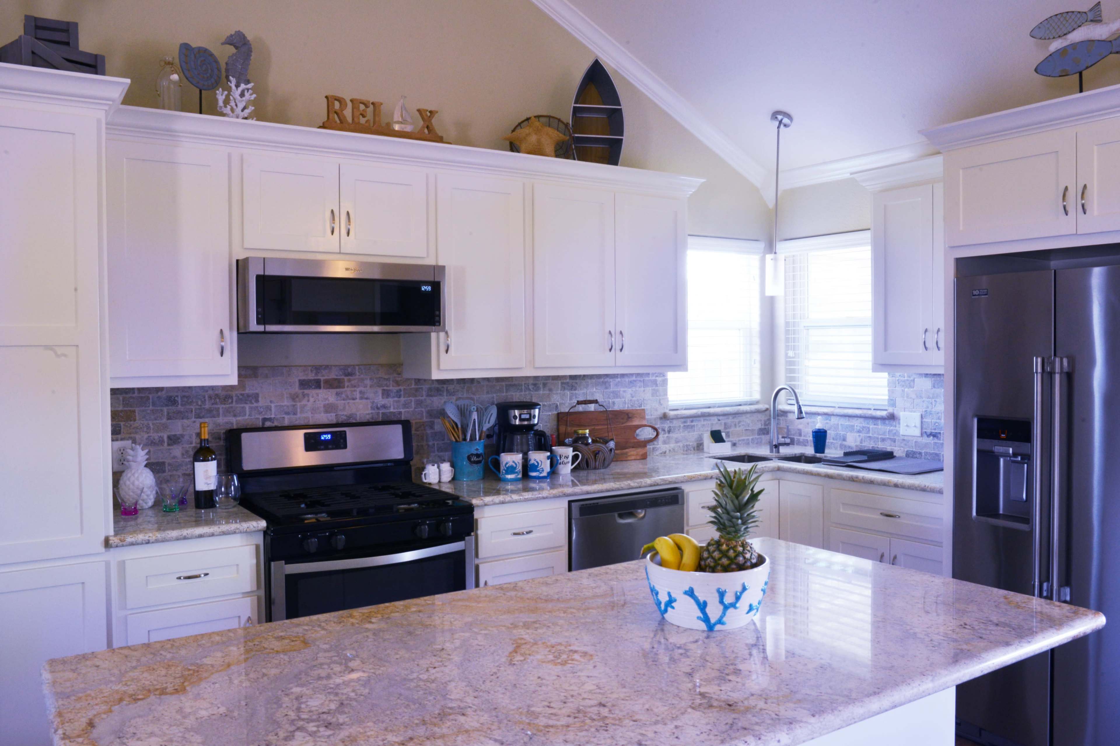 A modern kitchen features white cabinetry, stainless steel appliances, and a granite countertop with a bowl of fruit.