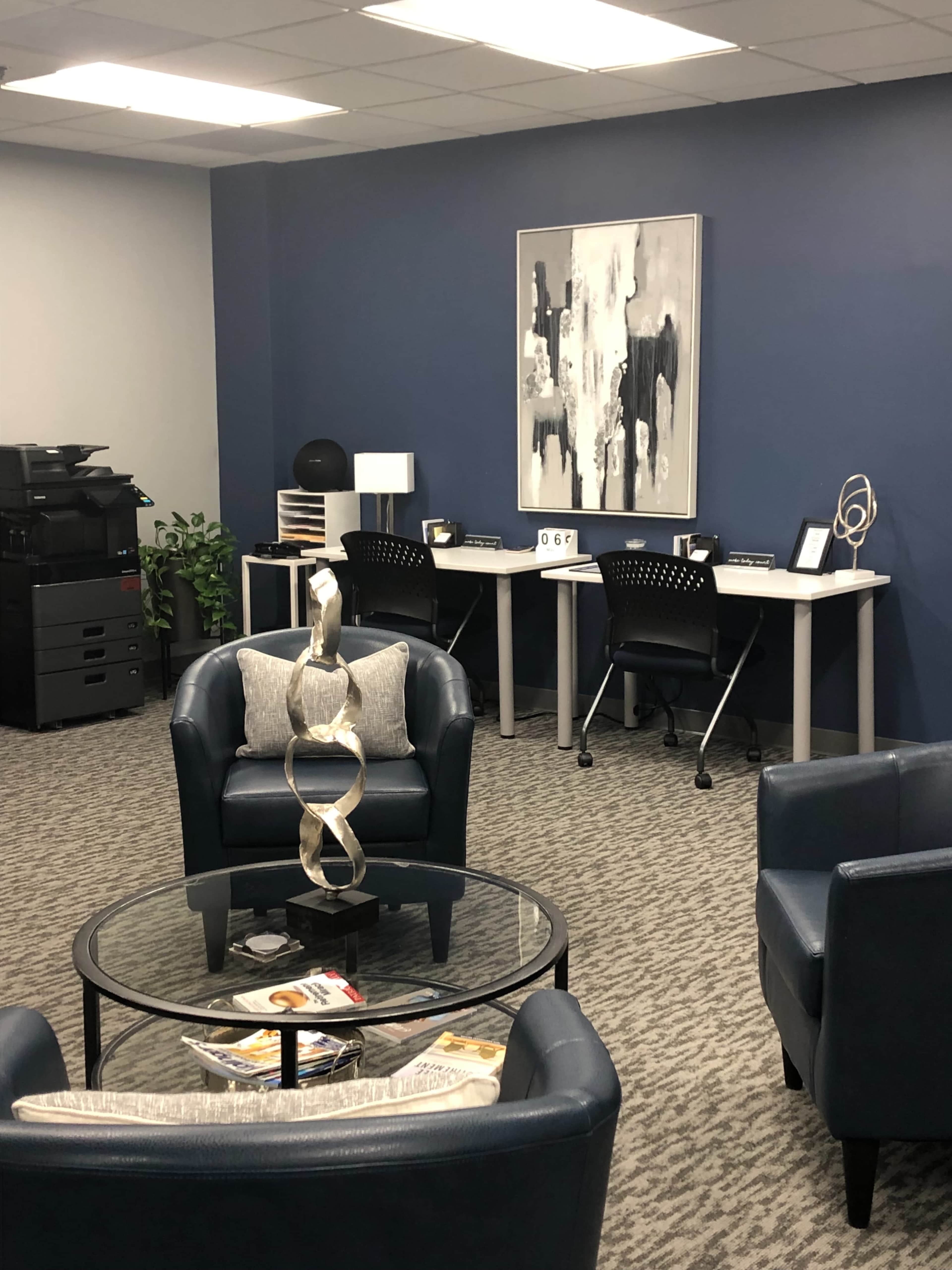 A modern office space with two desks, a coffee table, and seating arranged around the area.