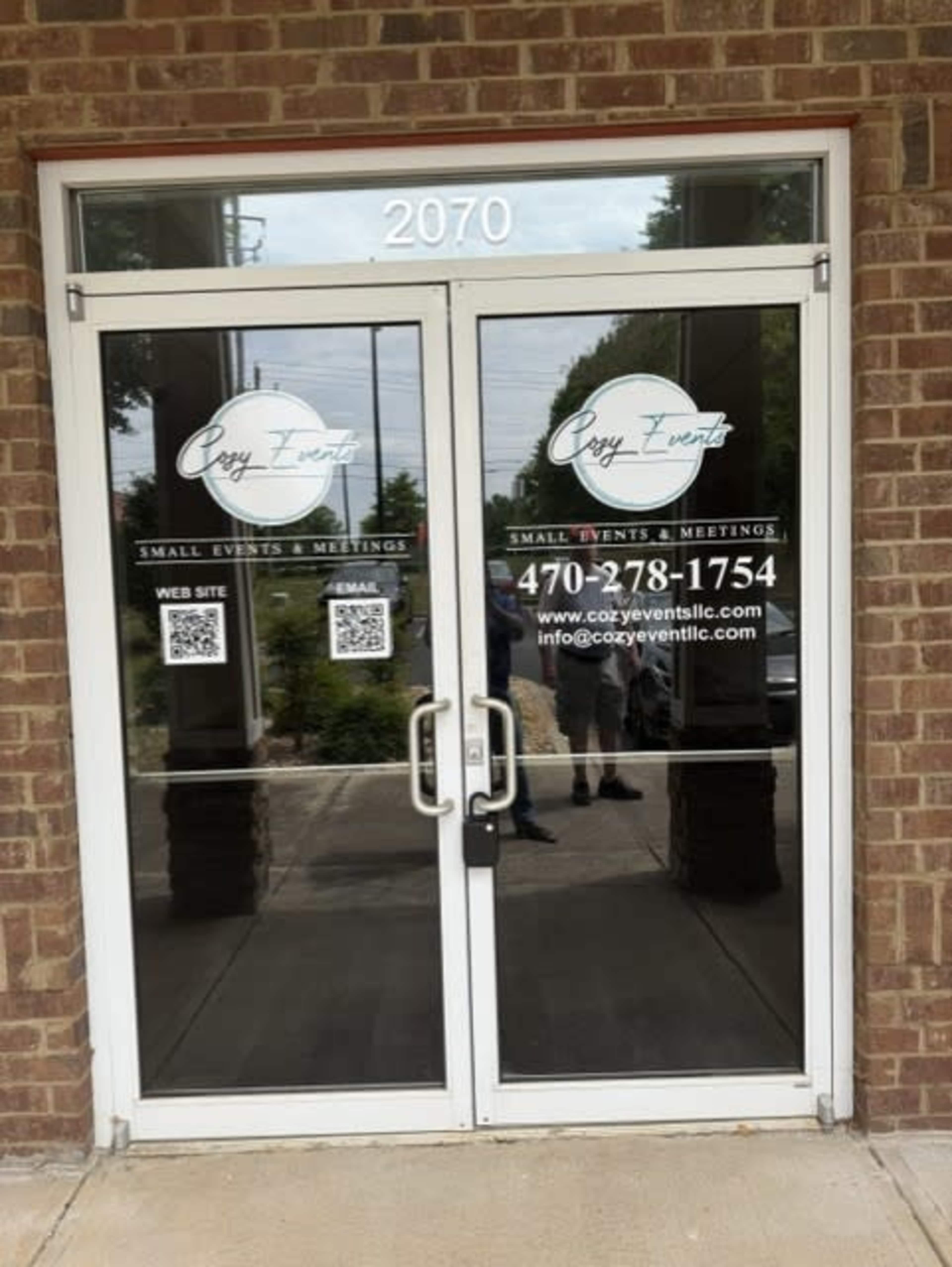 The image shows a glass double door entrance with the business name "Cozy Events" and contact information displayed prominently.