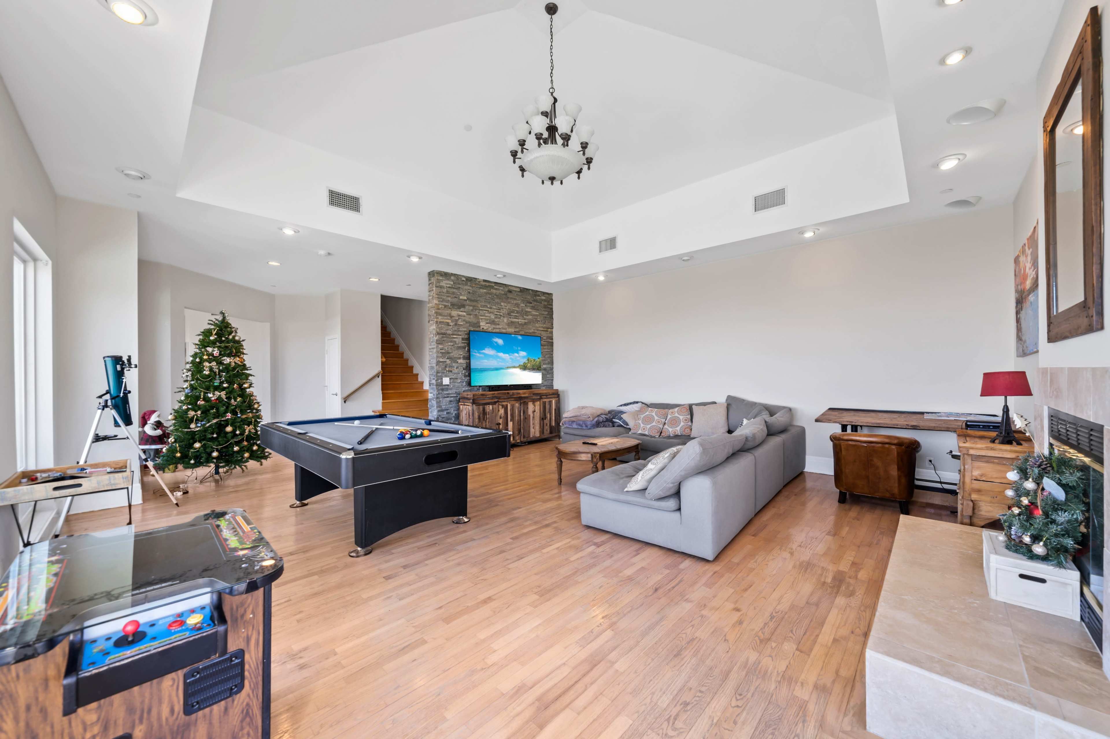 The image features a spacious living room with a billiard table, a large flat-screen TV, a Christmas tree, and a sofa.
