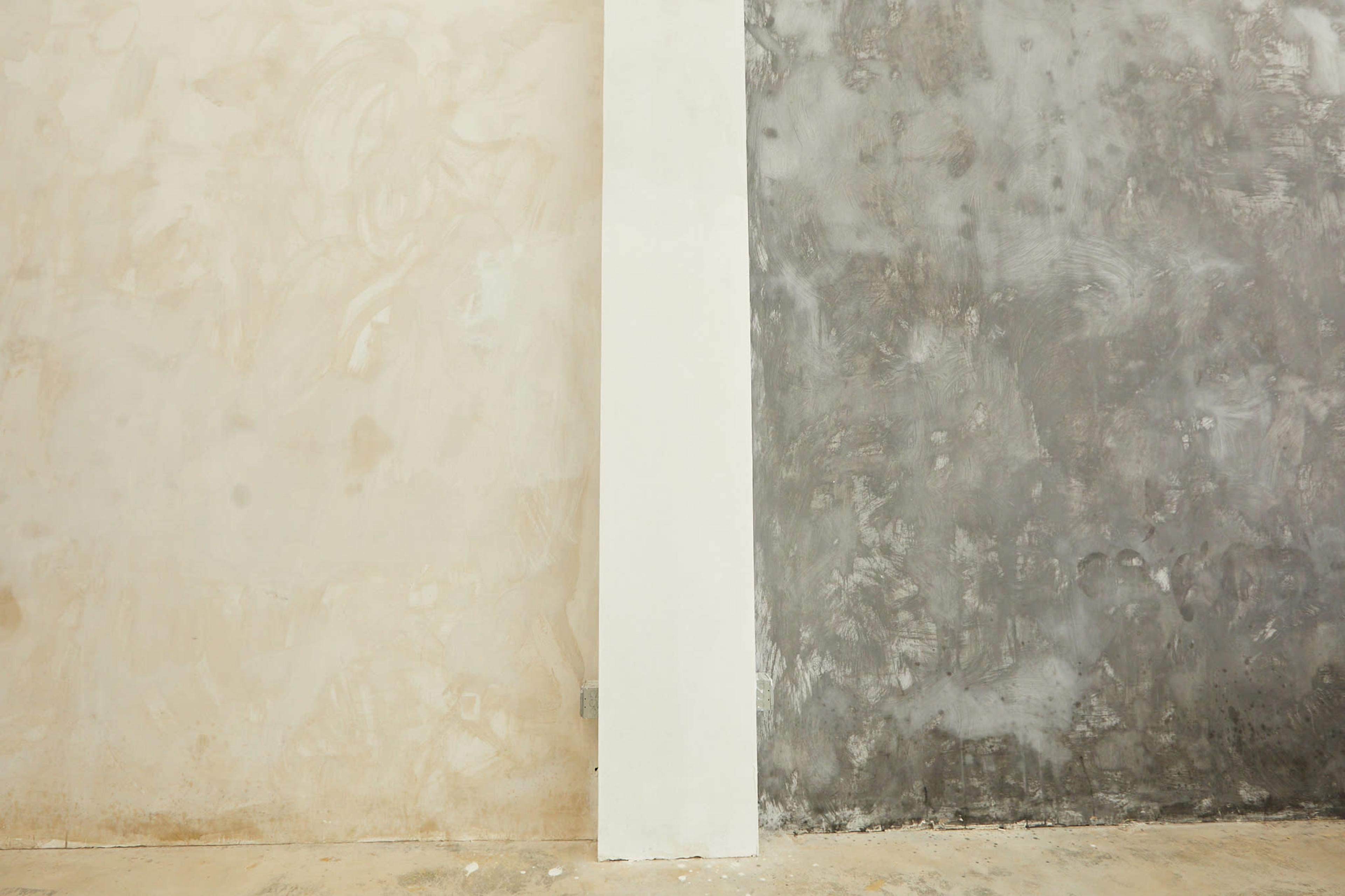 A divided wall with one side painted a light beige and the other side a textured gray.