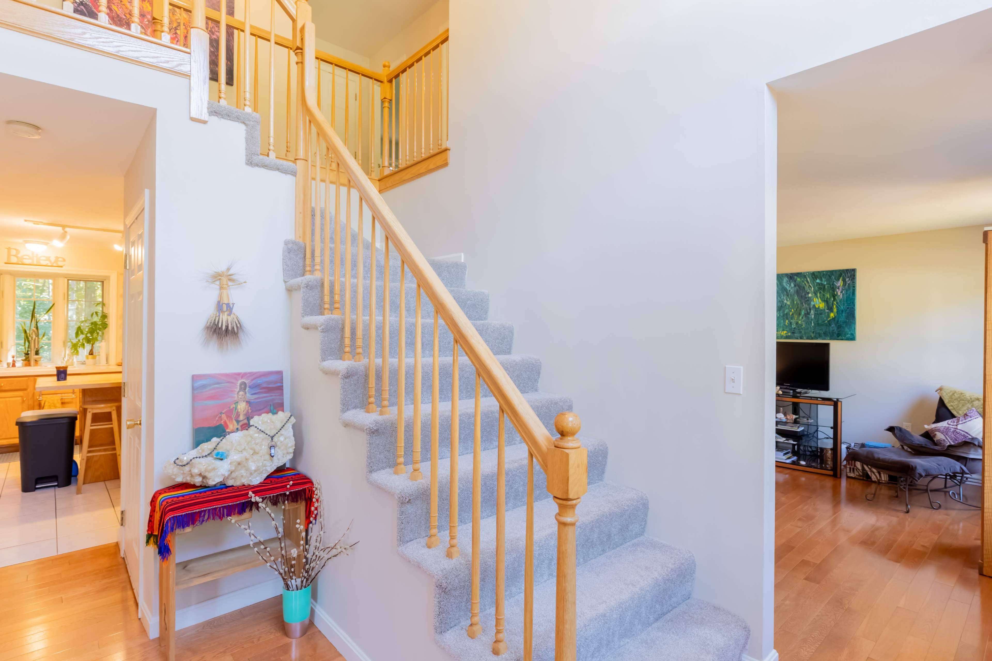 A well-lit entryway features a carpeted staircase leading to the upper level, with a small living area visible to the right.