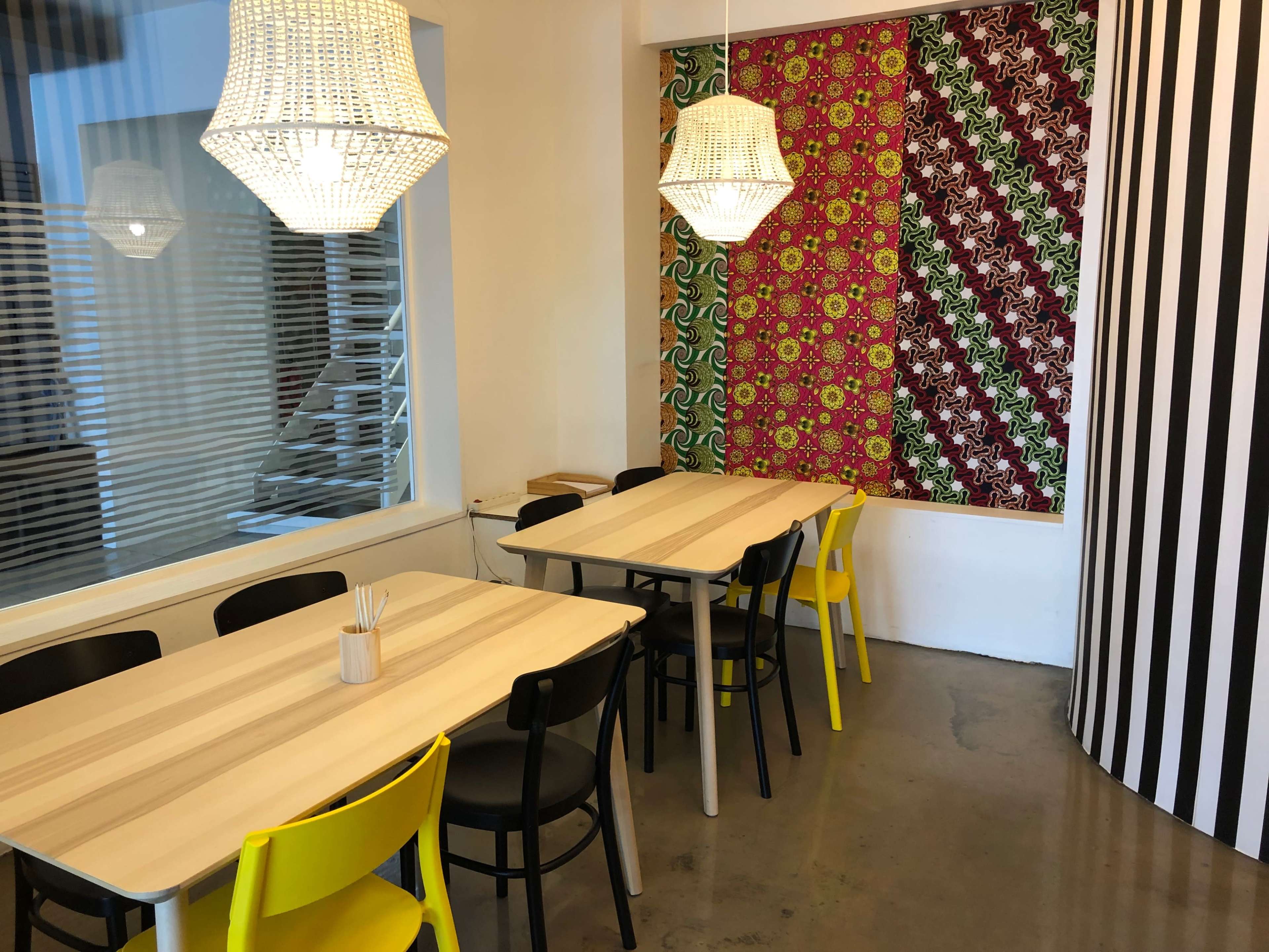 A brightly lit dining area with several wooden tables, black and yellow chairs, and patterned wall decor featuring bold colors.