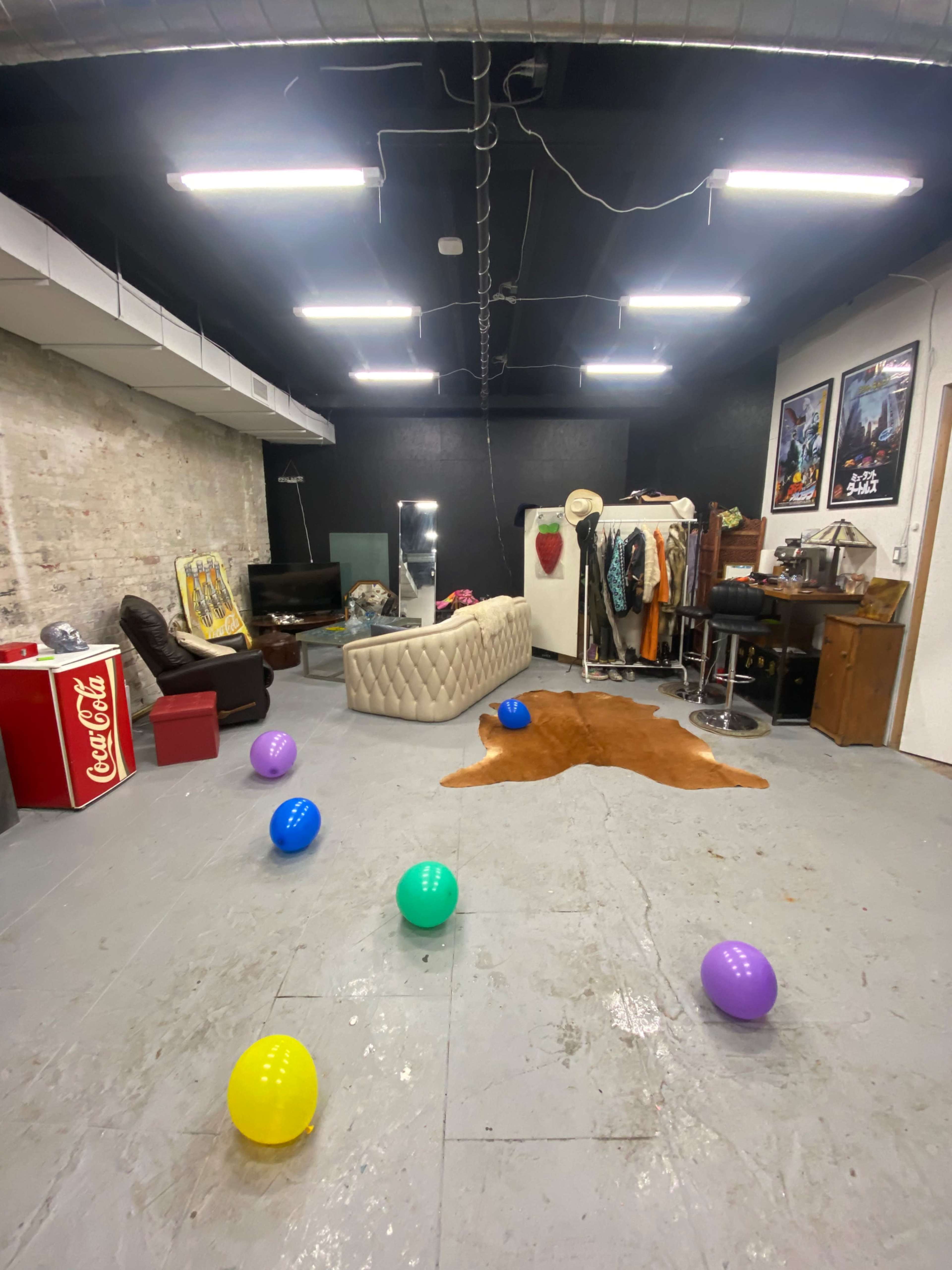 A spacious room features a couch, a mirror, a wardrobe, and colorful balloons scattered across the floor.