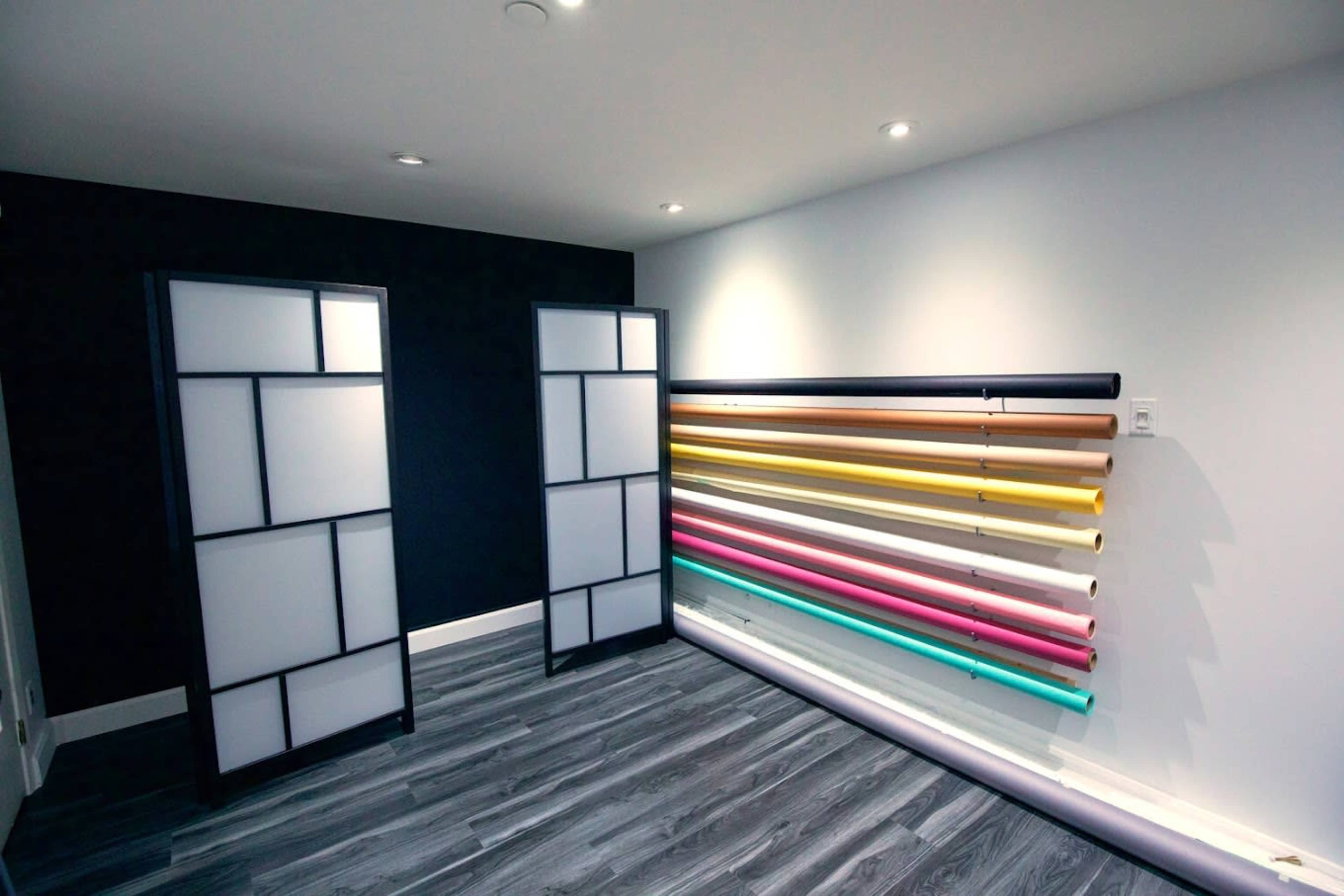 A room with two partition panels and a wall displaying a variety of colored rolls of paper.