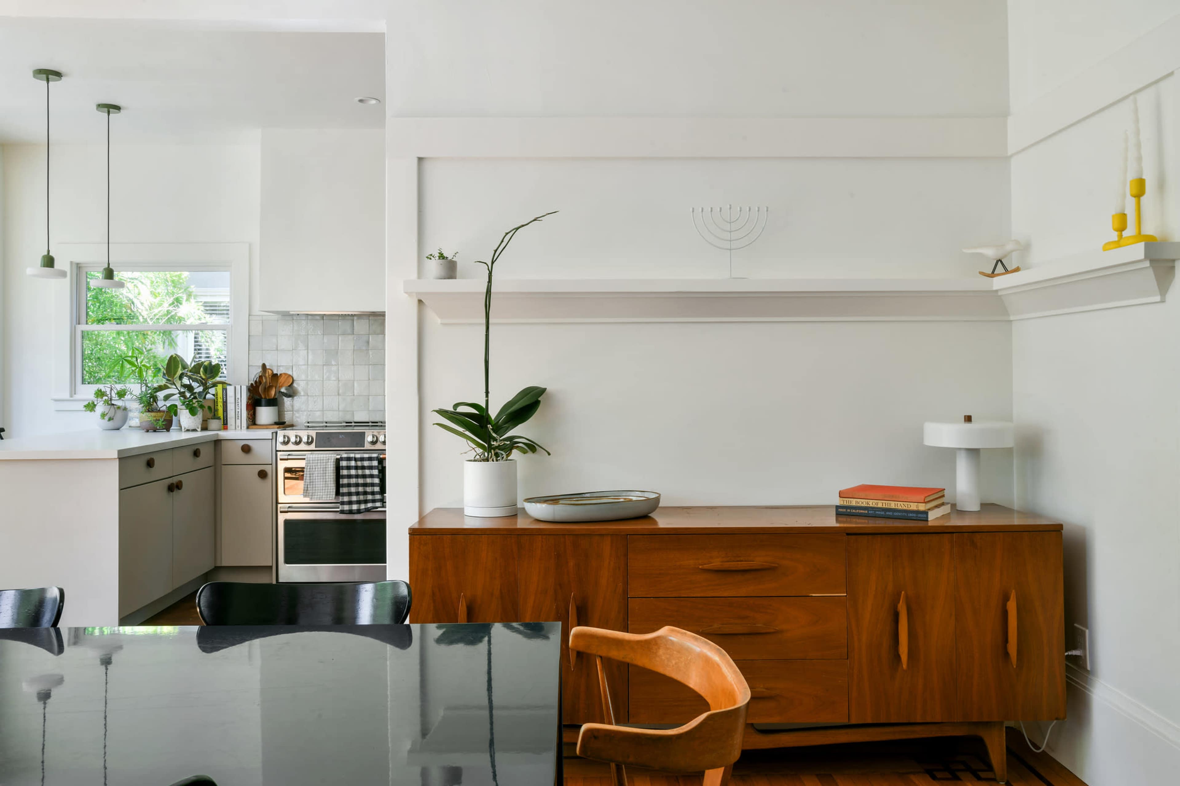 A bright kitchen and dining area featuring a wooden sideboard, a black dining table, and modern appliances.